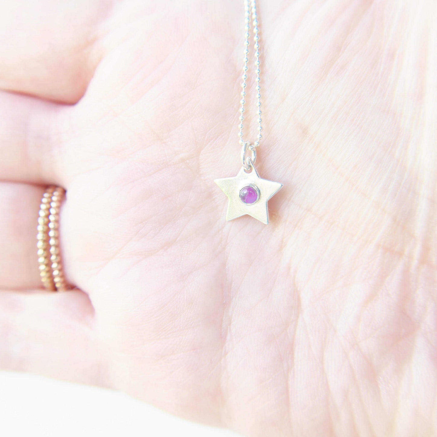 Small SIlver Star pendany with purple amethyst centre held in hand to show scale. It measures 12mm in size and is handmade in Scotland by Maram Jewellery