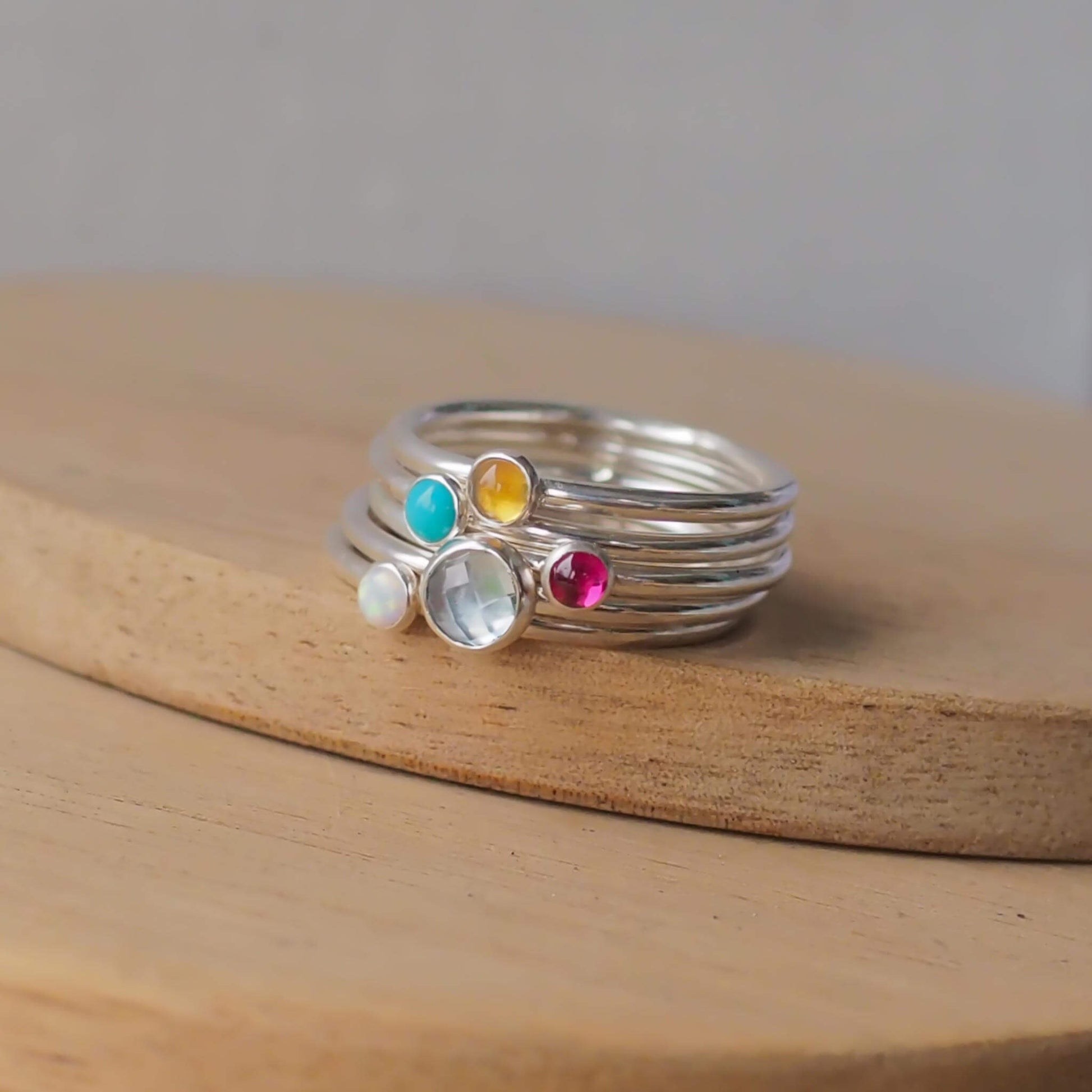 Five Ring Set with Blue Topaz, Citrine, Lab Ruby, Turquoise and Lab Opal to mark March, October November, December and July Birthdays. The five rings are made with Sterling Silver and a 5mm blue round cabochon, with four further rings with 3mm round gems in a iridescent white lab opal, yellow citrine, and a pinky red lab ruby. Handmade in Scotland by maram jewellery