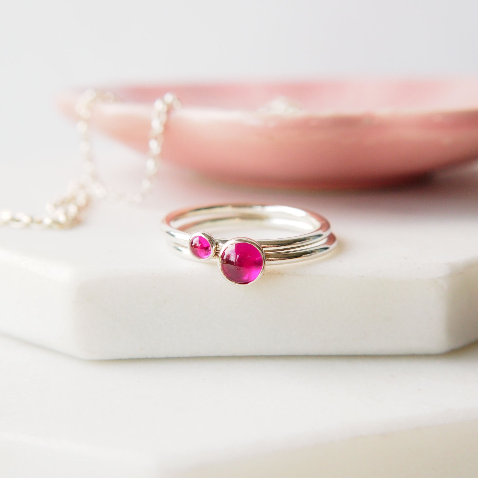 Double Ring set in Sterling Silver and hot pink Lab Ruby gemstones, The rings have two round gemstones of 5mm and 3mm size and are set simply onto round bands of sterling silver. These are July's birthstone and are handmade to your ring size by maram jewellery in Scotland