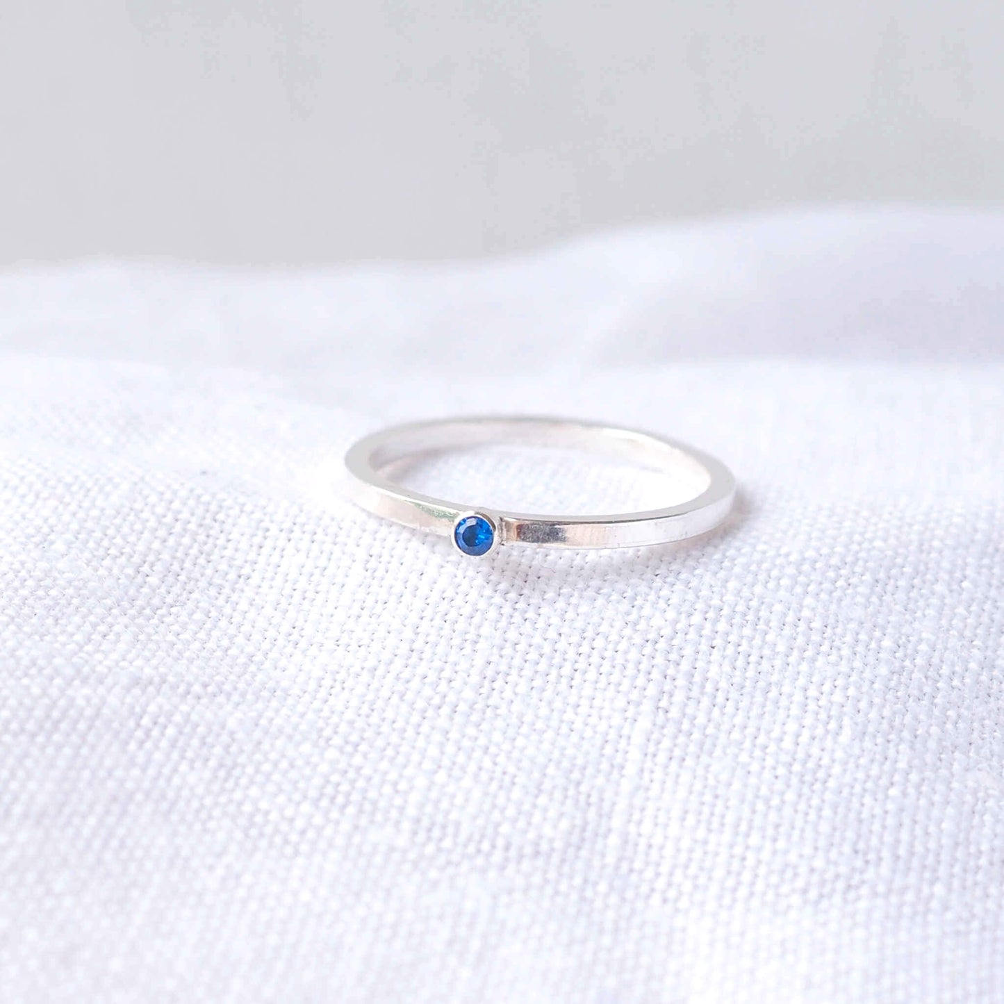 Silver and Blue Cubic Zirconia ring on a modern round square band with a small gemstone. The gem is a 2mm round cubic zirconila with pleny of sparkle. Handmade in Scotland by maram jewellery