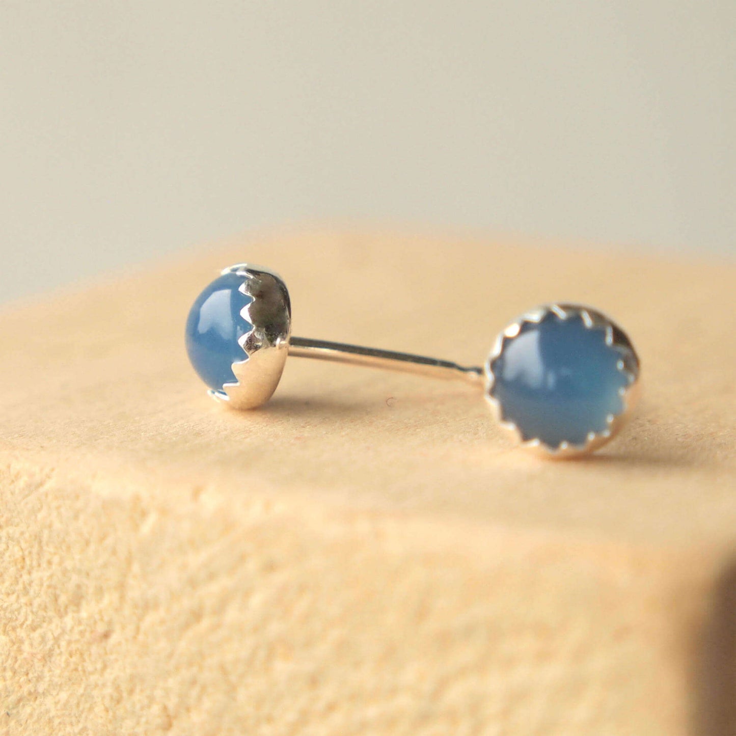 simple minimalist style Silver round gemstone earrings, handmade by maram jewellery in Scotland UK. The 5mm sized round earrings are simple in design, set into a sterling silver mount with a zig zag edge, Sterling Silver and Blue Agate gemstones.