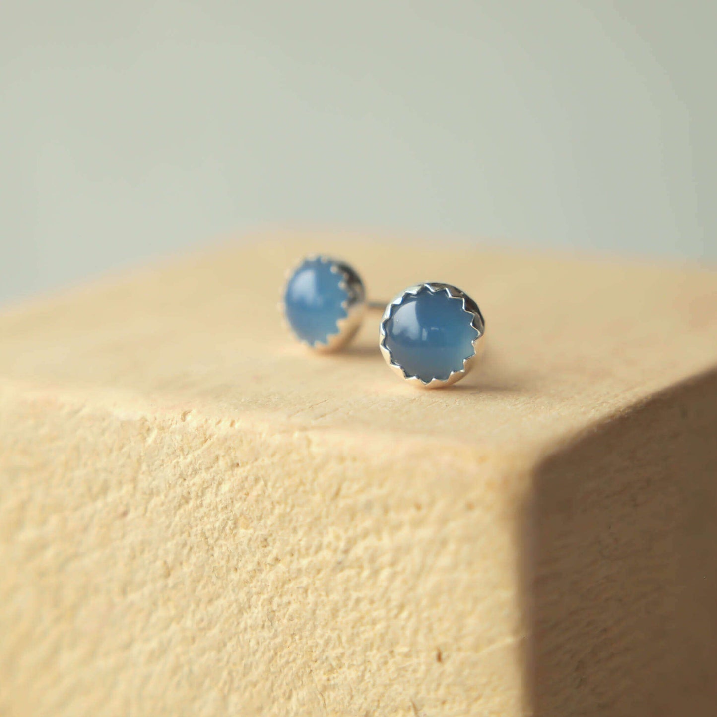 Silver round gemstone earrings, handmade by maram jewellery in Scotland UK. The 5mm sized round earrings are simple in design, set into a sterling silver mount with a zig zag edge, Sterling Silver and Blue Agate gemstones.