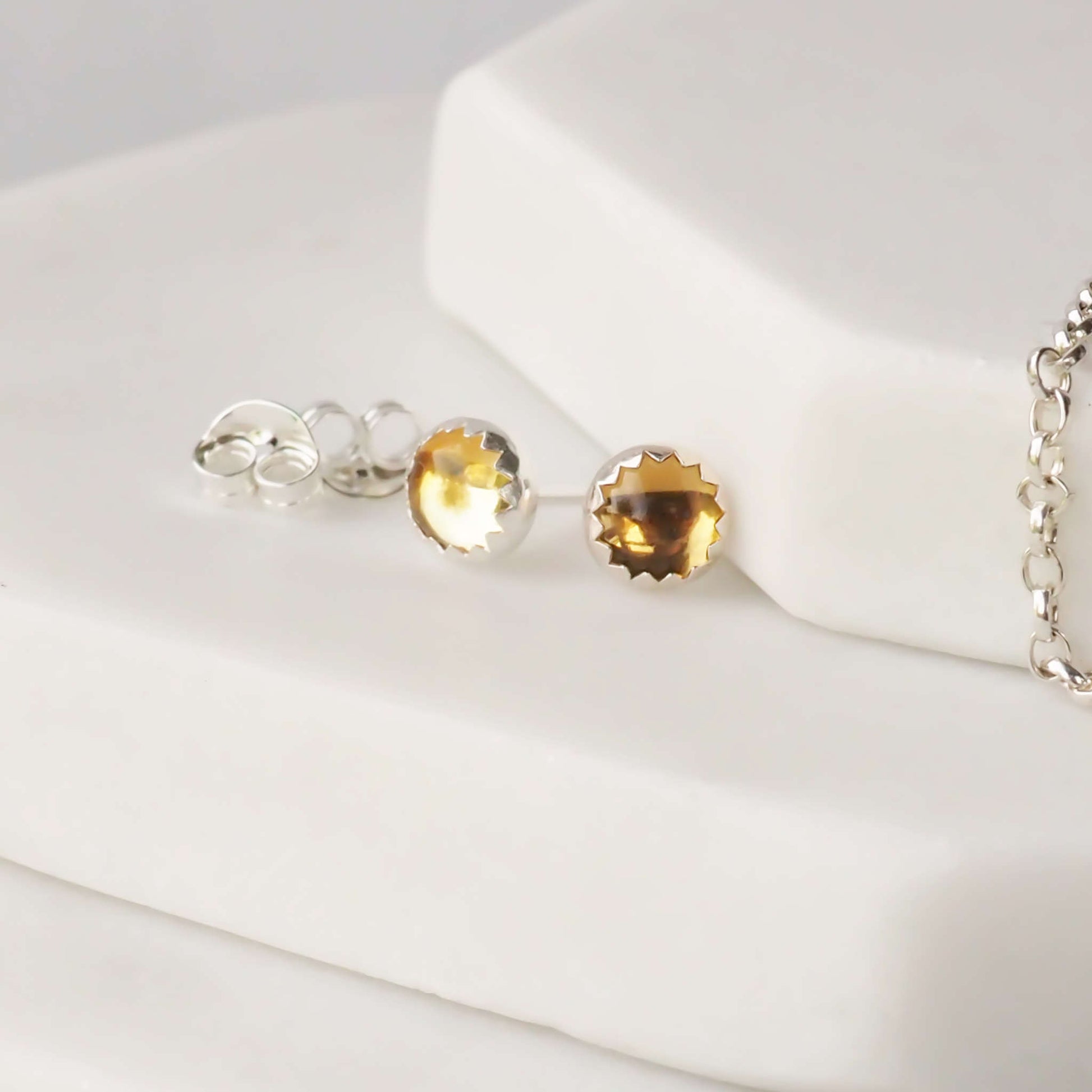 citrine earrings sitting on a hexagonal marble surface. The earrings are made from round cabochons measuring 5mm in a warm yellow citrine, birthstone for November. They are handcrafted by maram jewellery, a small indie business based in Edinburgh UK