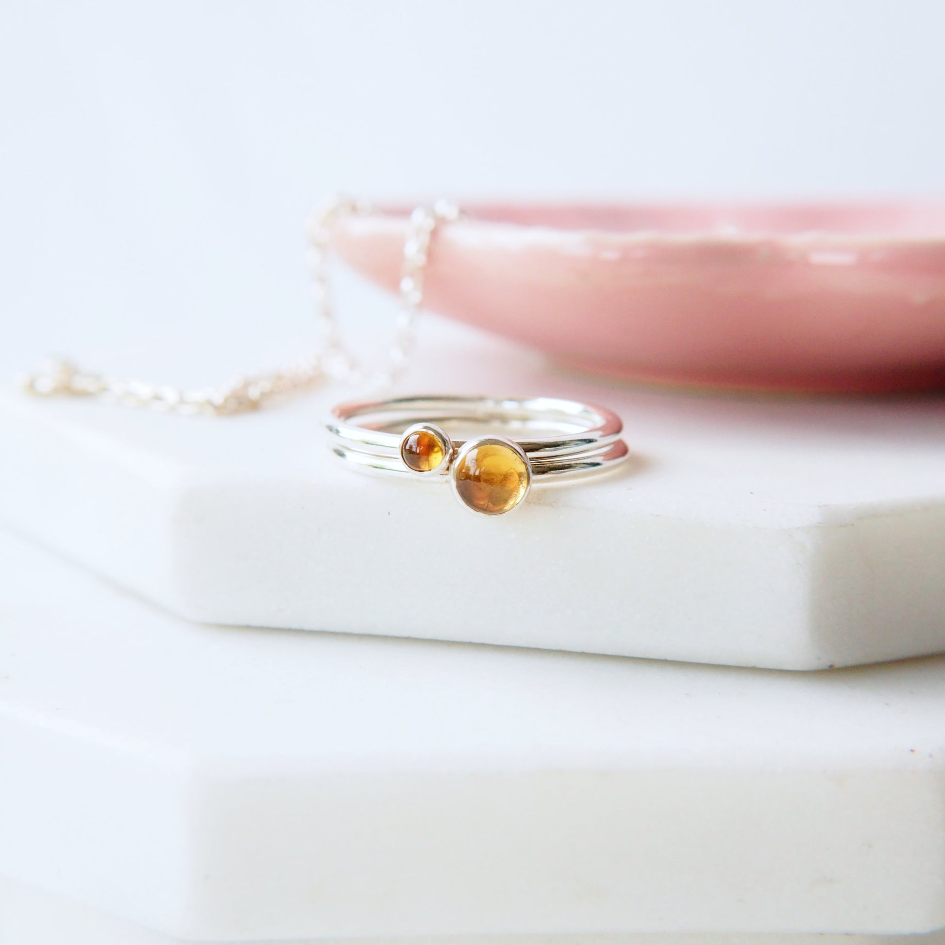 Two ring set with different sized round citrine gemstones. silver with yellow gemstones pictured in  a white background with a pink bowl. Made by maram jewellery in Scotland