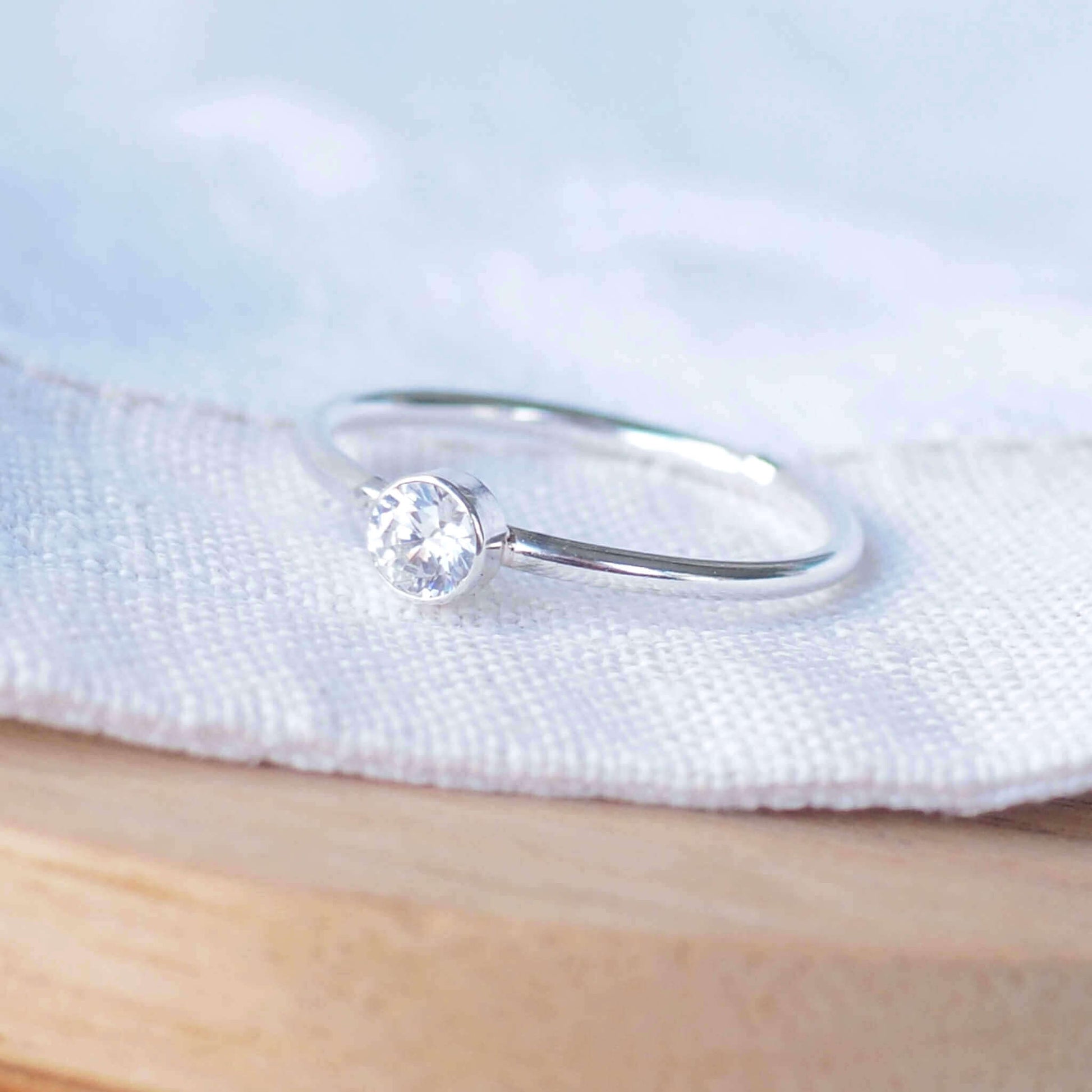 Sparkly imitation diamond ring on white metal. Sterling Silver and Cubic zirconia ring made in a simple solitaire style with a 4mm round gemstone modern set in a fully enclosed surround. Handmade in Scotland by maram jewellery