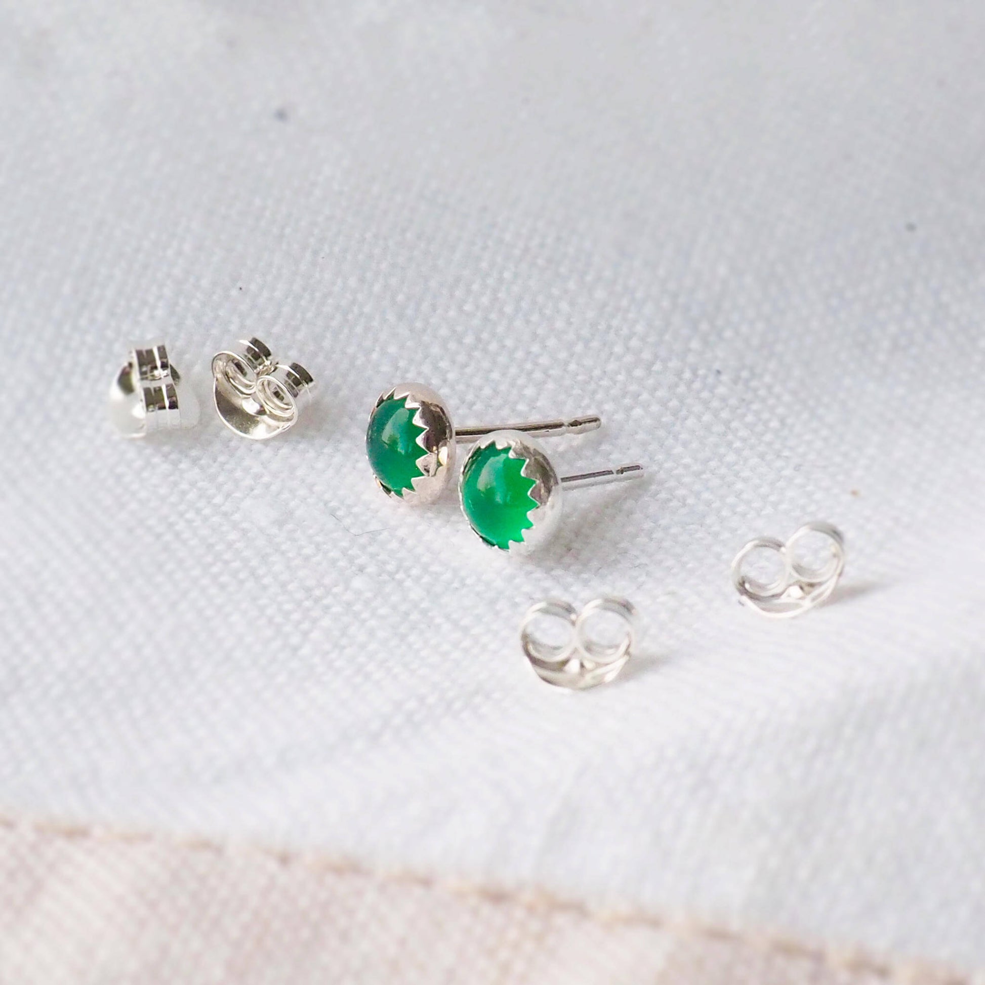 Modern styled emerald green birthstone earrings with a minimalist look. made from sterling silver and green agate, these are simple style earrings pictures on a neutral linen backdrop