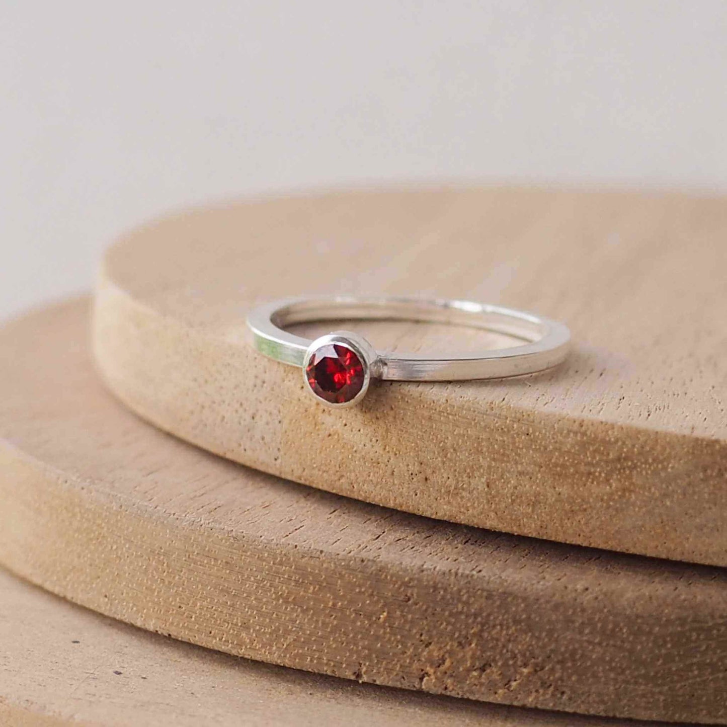 Garnet and Sterling Silver solitaire ring with a dark red coloured round cubic zirconia measuring 4mm in size. A very simple minimalist ring made from Sterling Silver on a minimalist square style band.Garnet is the birthstone for January. Handmade in Scotland by maram jewellery
