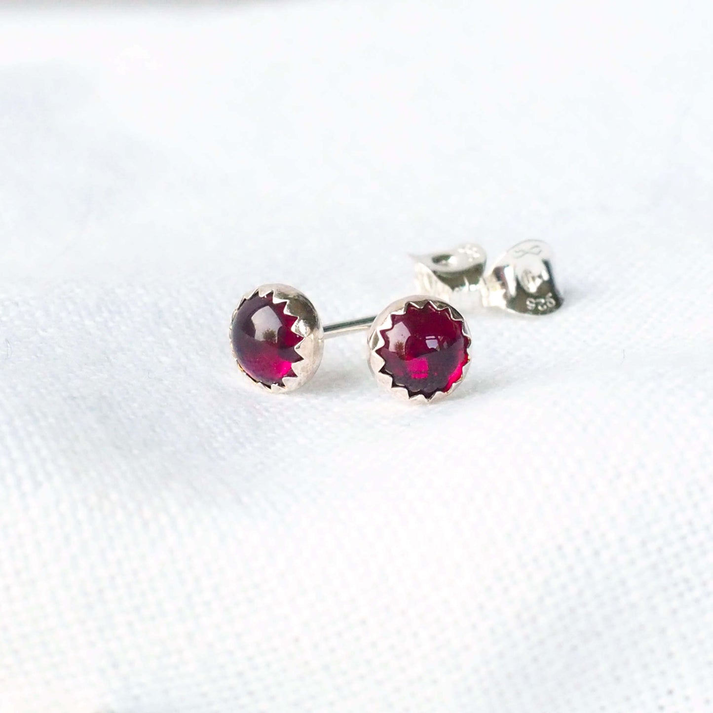 Simple Modern Gemstone stud earrings in sterling silver and round garnet. The earrings measure 5mm in size and are very simply set with a unusual wavy edge. Handmade in Scotland by a small independent jeweller called maram jewellery
