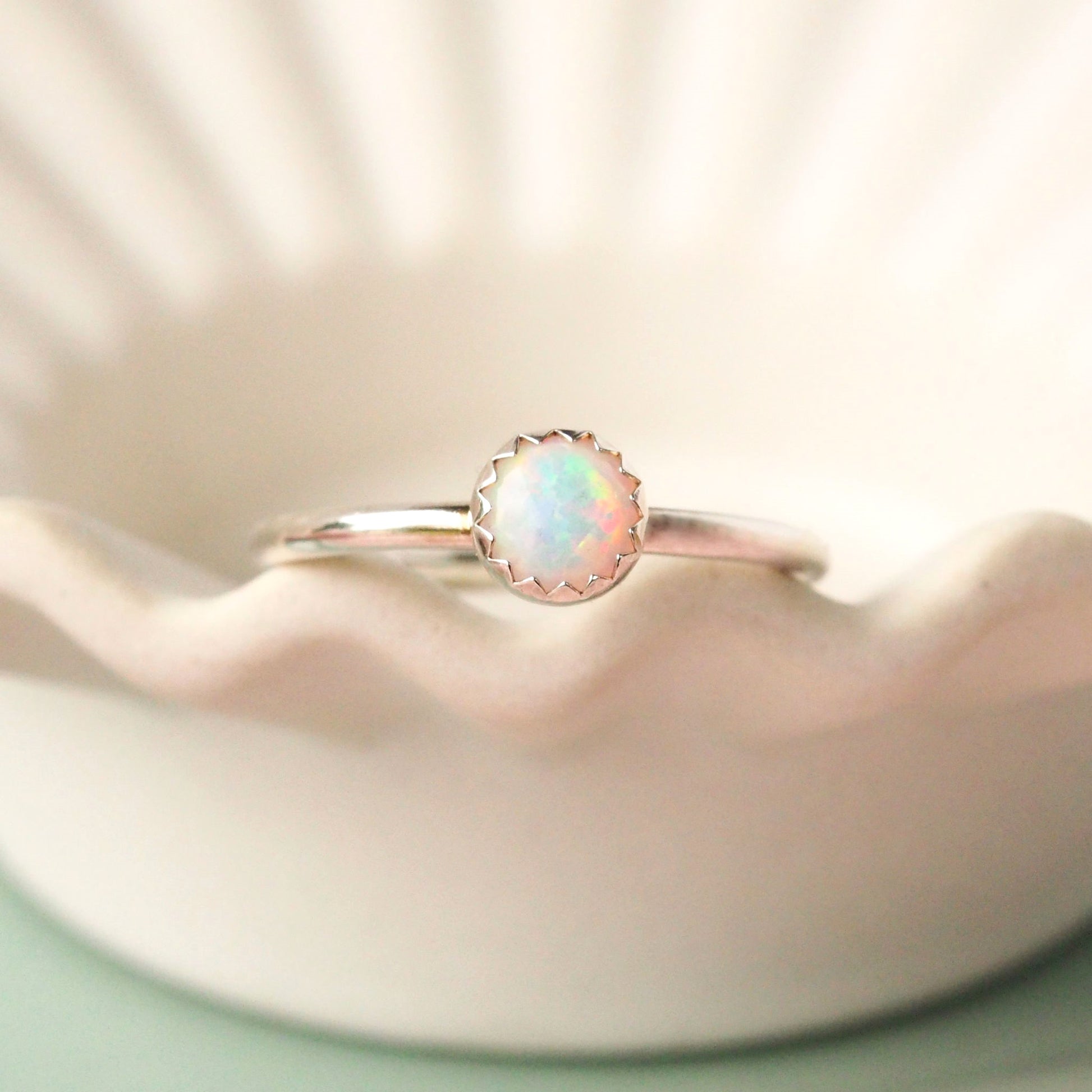Silver and Opal Birthstone Ring for October on a white wavy edge plate. The ring in made from Sterling silver with a modern halo band and a white shimmery round lab opal measuring 5mm. It is handmade by maram jewellery in Edinburgh UK