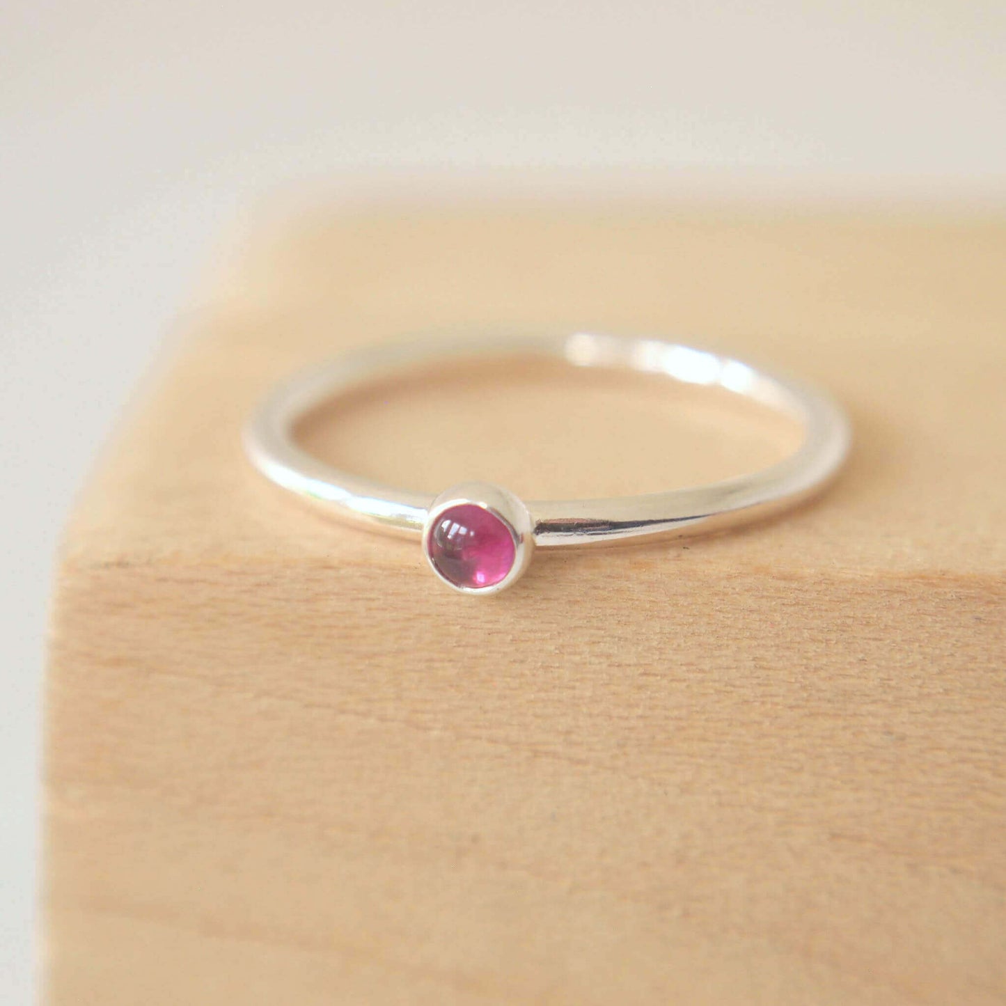 Silver ring with a pink gemstone on a wooden surface