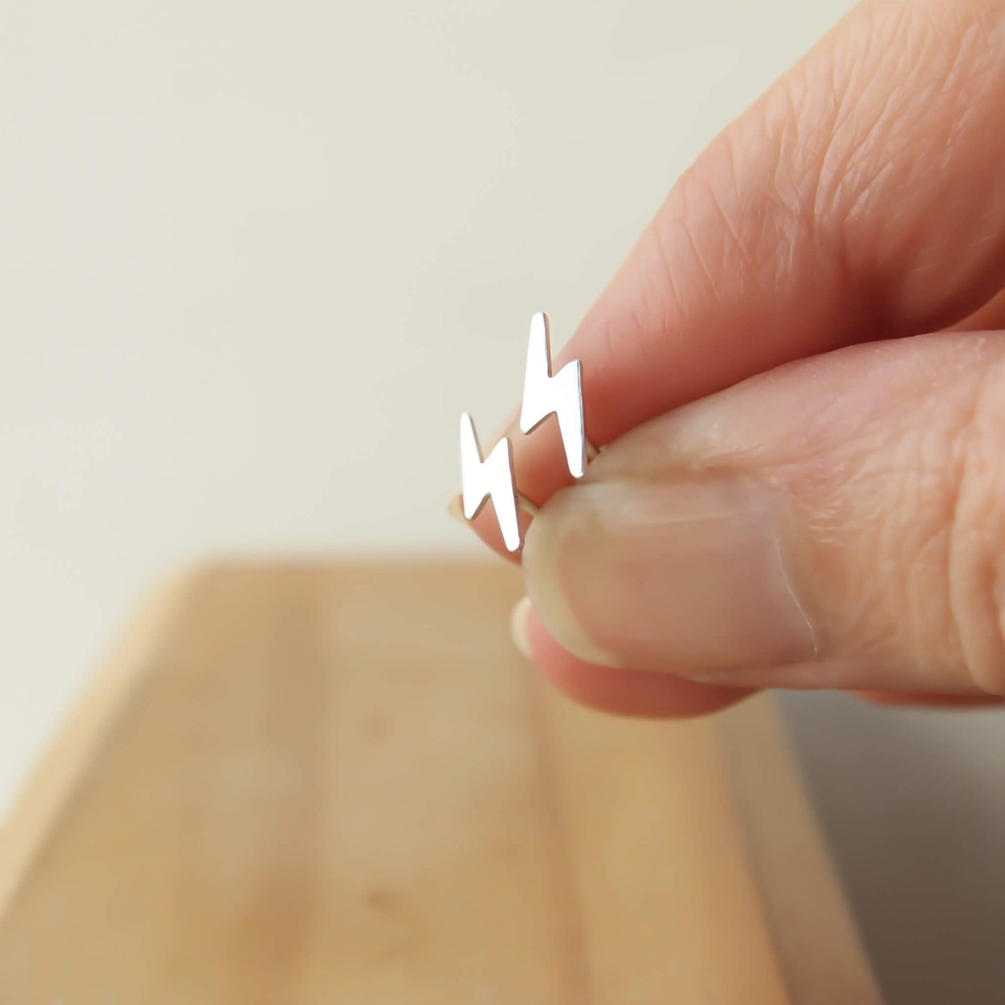 Sterling SIlver lightning bolt earring worn pictured on a wooden background. handmade by maram jewellery in Edinburgh UK