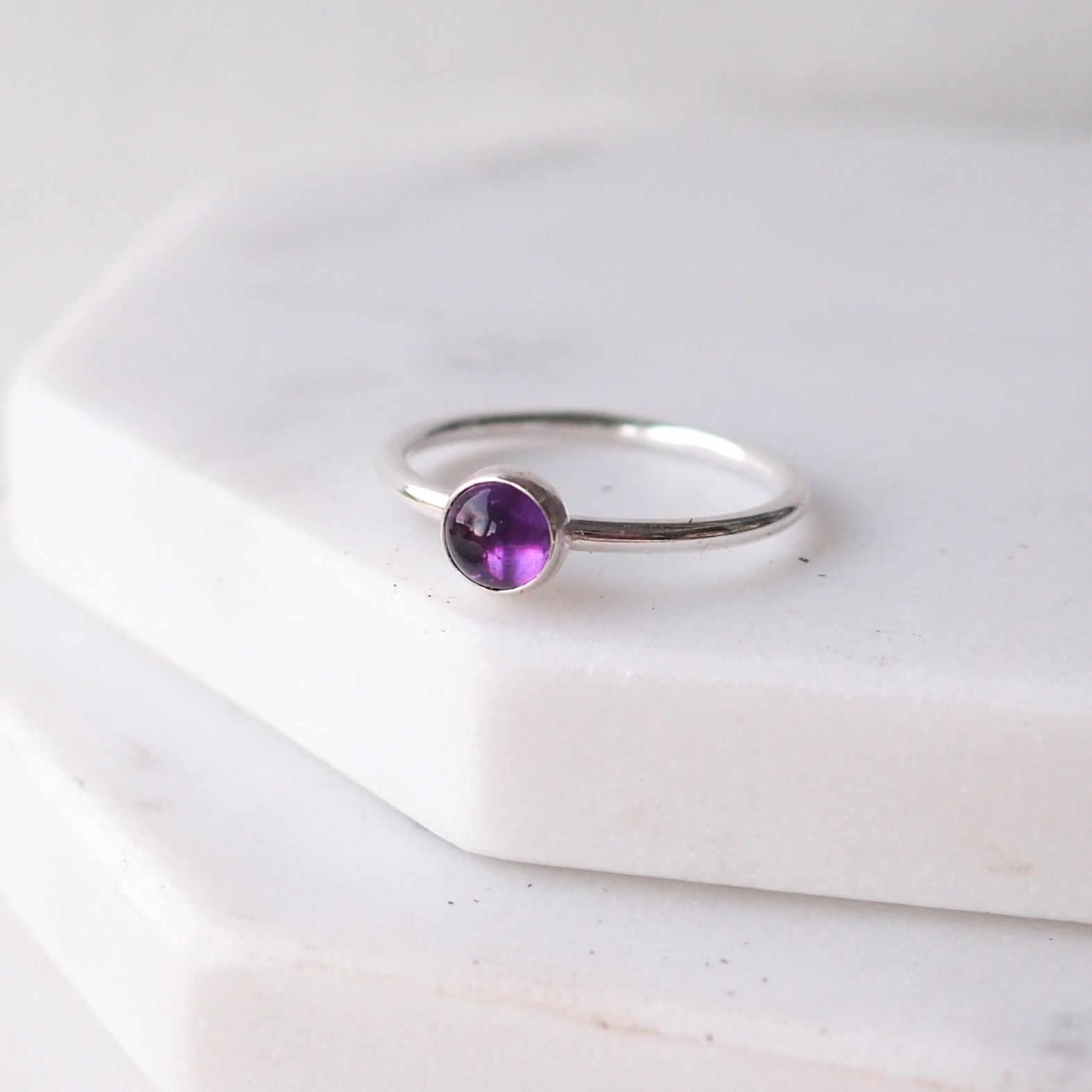 Single solitaire sterling silver ring with a round 5mm purple Amethyst. The ring is made in a modern simple style with a 5mm round cabochon set onto a modern halo fully round band. Made to order to your ring size, and handmade in Scotland by maram jewellery