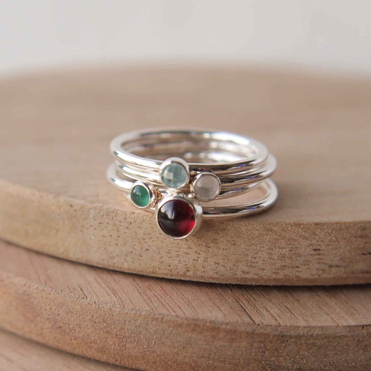 Birthstone ring set with four stones to mark family birthstones. image contains rings in sterling silver with a red garnet, green agate, white moonstone and blue topaz. Handmade by maram jewellery in Scotland UK