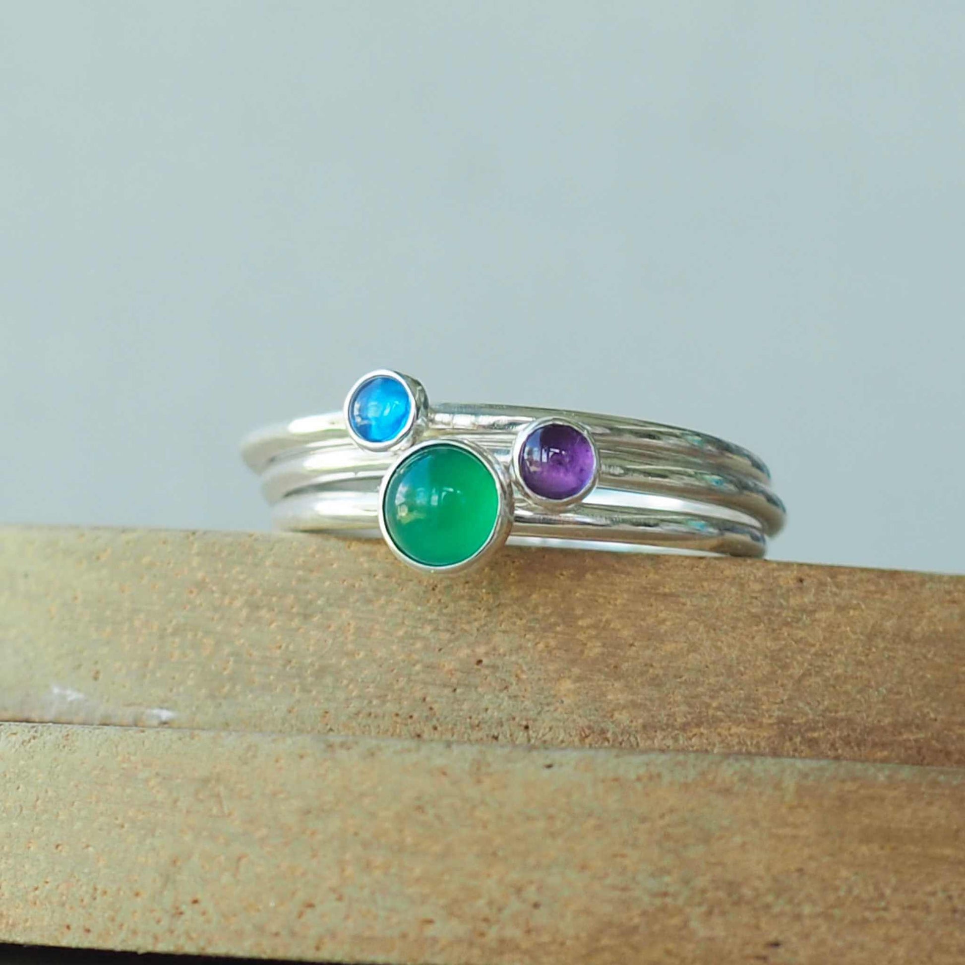 Three Birthstone Ring set made from Sterling Silver, with a 5mm round Green Agate Birthstone for May, and two smaller 3mm gemstones in Lab Sapphire for September and Amethyst for February. The gemstones colours are emerald green, purple and primary blue. Handmade in Scotland by Maram Jewellery