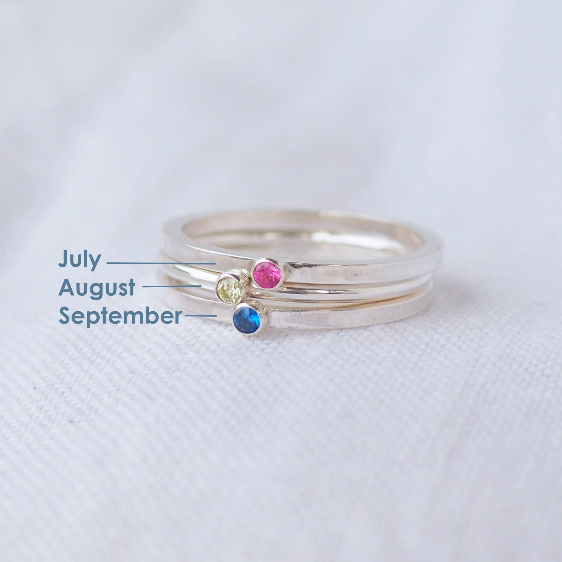 Three silver rings showing July,August and September  Birthstones. The rings are simple silver bands with a miniature birthstone on the band in pink,moss green and blue cubic zirconia. Handmade in Edinburgh by maram jewellery