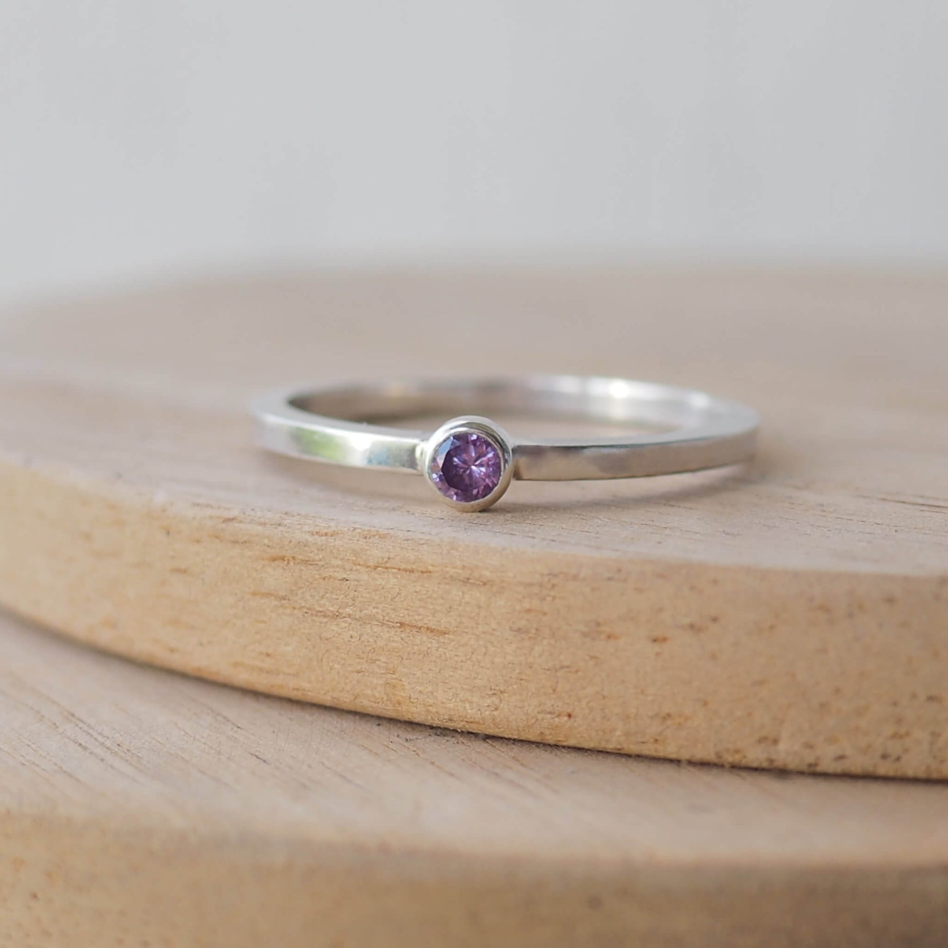 Silver ring with a purple gemstone. The ring is simple in style with no embellishment , with a square wire band 1.5mm thick with a simple purple 3mm round cubic zirconia stone set in an enclosed silver setting. Amethyst is birthstone for February. The ring is Sterling Silver and made to your ring size. Handmade in Scotland by Maram Jewellery