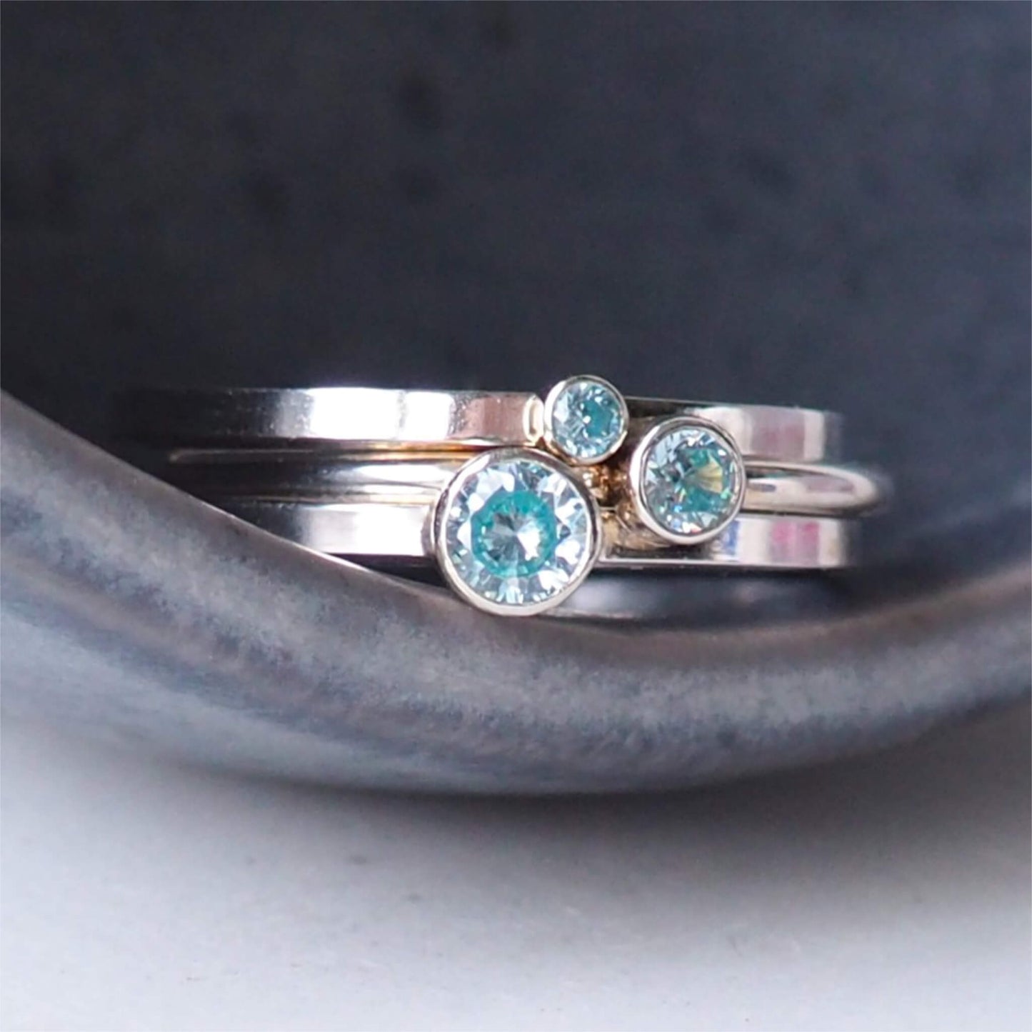 Set of three Aquamarine cubic zirconia rings stacked in a grey ceramic bowl. Handmade by maram jewellery in Scotland UK