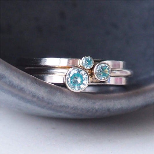 Set of three Aquamarine cubic zirconia rings stacked in a grey ceramic bowl. Handmade by maram jewellery in Scotland UK