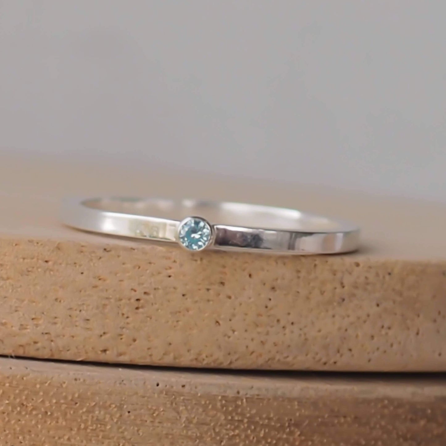 Silver ring with a light aqua gemstone. The ring is simple in style with no embellishment , with a square wire band 1.5mm thick with a simple Pale Blue Aquamarine 2mm round cubic zirconia stone set in an enclosed silver setting. Aquamarine is the birthstone for March. The ring is Sterling Silver and made to your ring size. Handmade in Scotland by Maram Jewellery