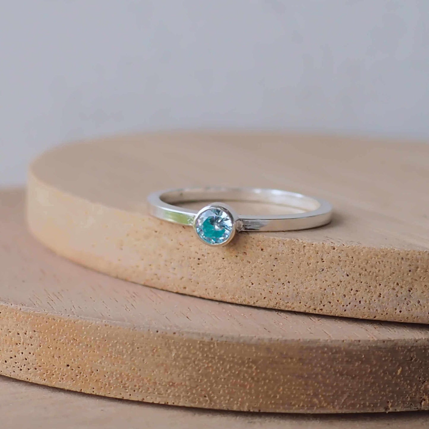 Silver ring with a light aqua gemstone. The ring is simple in style with no embellishment , with a square wire band 1.5mm thick with a simple Pale Blue Aquamarine 4mm round cubic zirconia stone set in an enclosed silver setting. Aquamarine is the birthstone for March. The ring is Sterling Silver and made to your ring size. Handmade in Scotland by Maram Jewellery