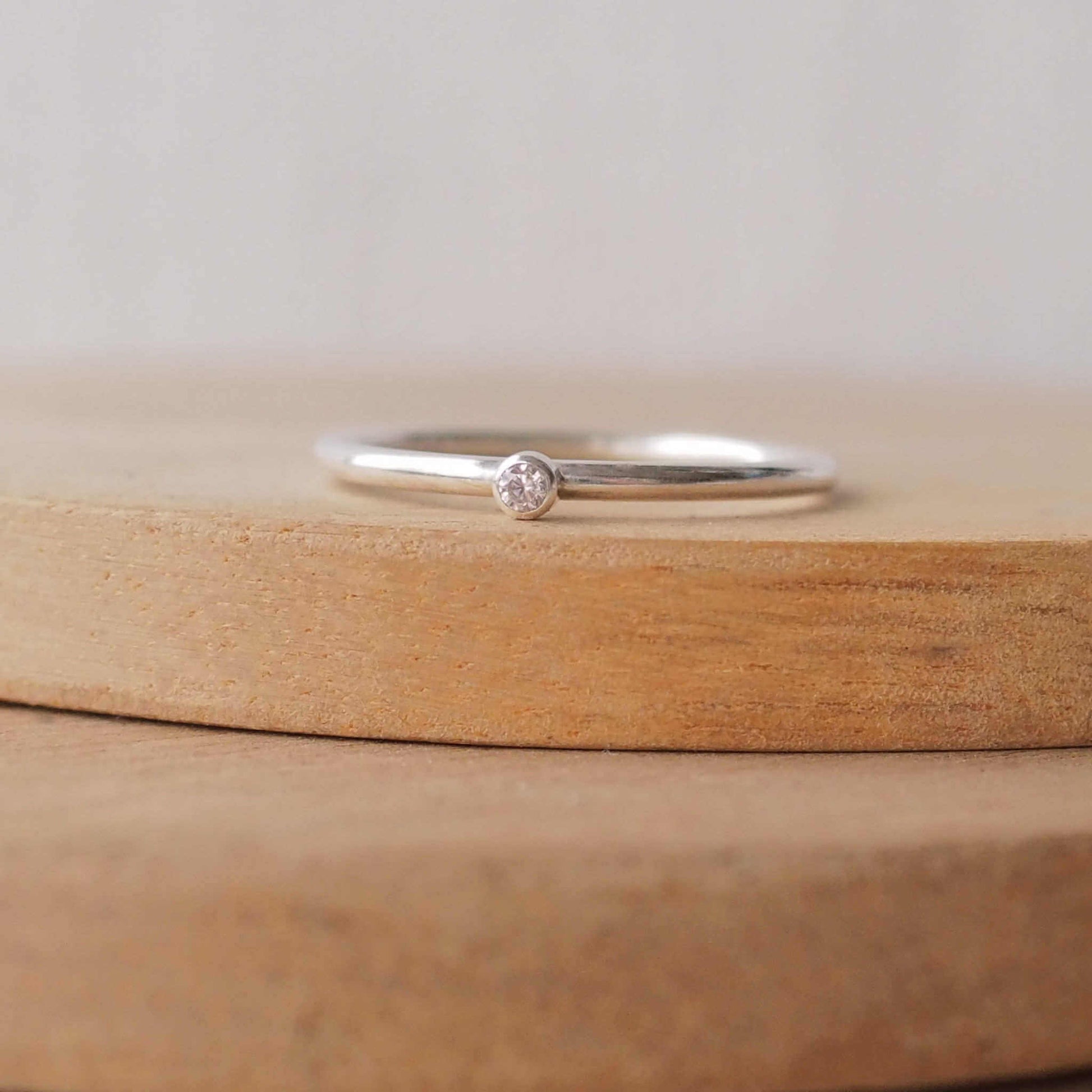 Imitation Diamond and silver minimalist solitaire ring. Made from a modern band of round silver wire with a simple round faceted cubic zirconia. The stone is tiny and understated at 2mm, round in shape and clear in colour, and is set in a fully enclosed silver surround. Handmade in Scotland by Maram Jewellery