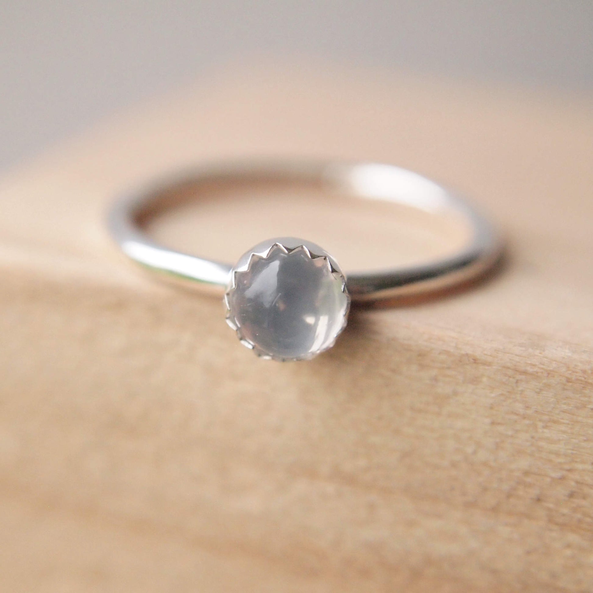 Sterling silver and moonstone cabochon ring. 5 mm sized milky white cabochon stone on a fully round band of sterling silver with a zig zag edge where the stone meets the band. Handmade in Scotland by maram jewellery