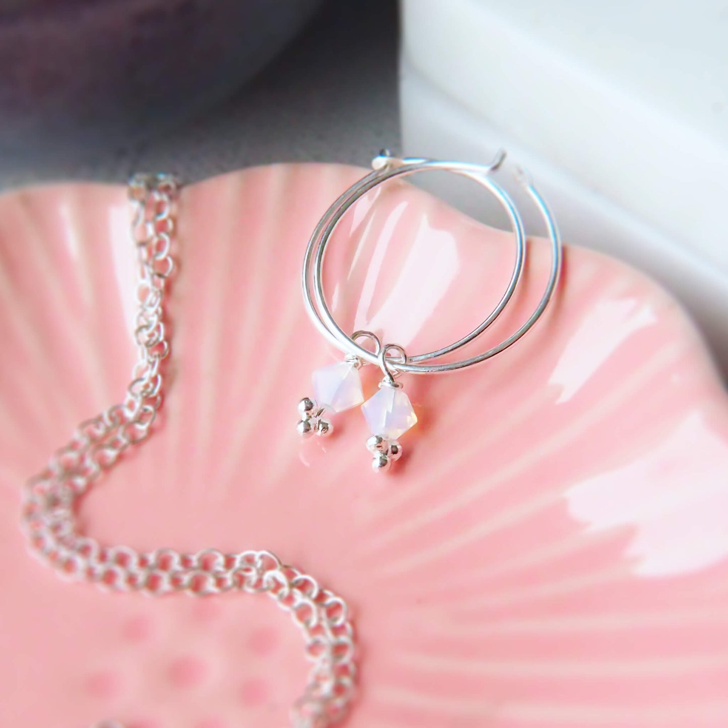 Maram Jewellery birthstone crystal earrings with opal lustre crystal. the earrings are a thin sterling silver full hoop, 2 cm diameter with a milky iridescent white crystal charm drom for October's Birthstone. handmade in Scotland
