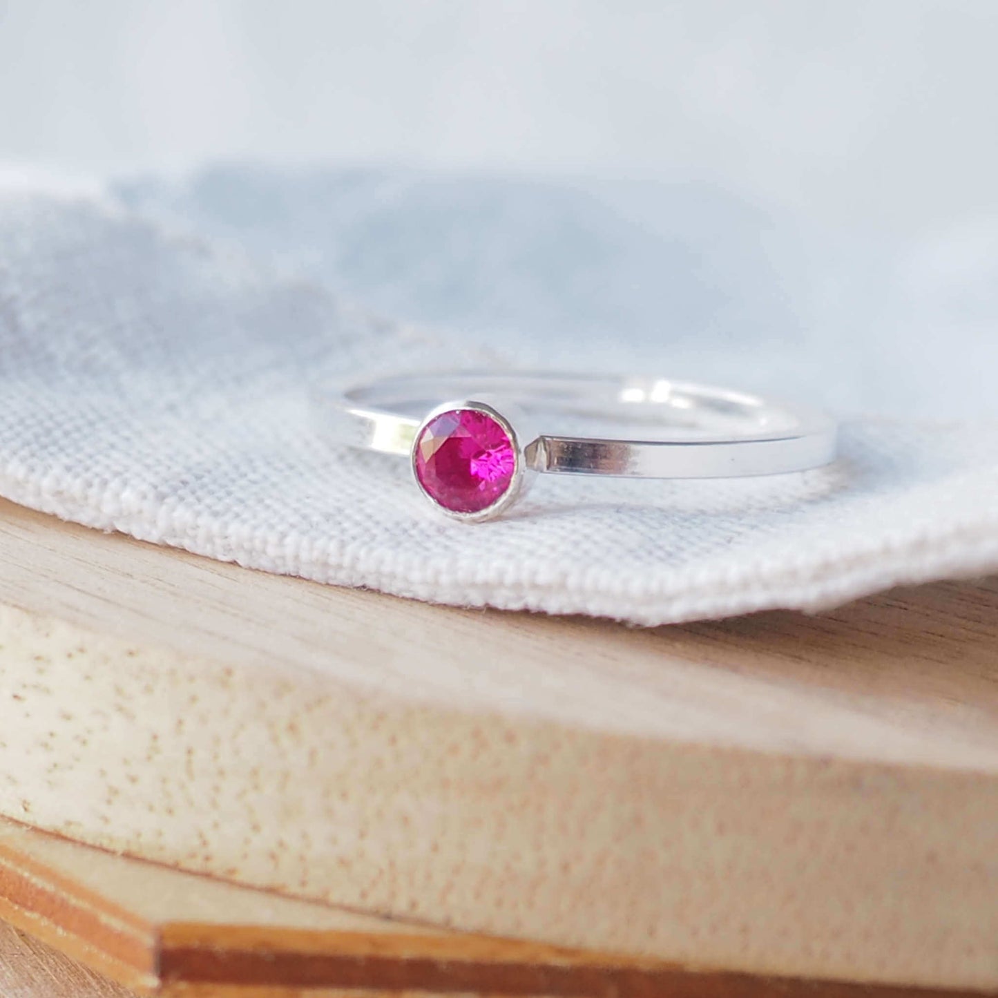 Silver ring with a pinky red gemstone. The ring is simple in style with no embellishment , with a round wire band 1.5mm thick with a simple ruby coloured 4mm round cubic zirconia stone set in an enclosed silver setting. Ruby is birthstone for July. The ring is Sterling Silver and made to your ring size. Handmade in Scotland by Maram Jewellery