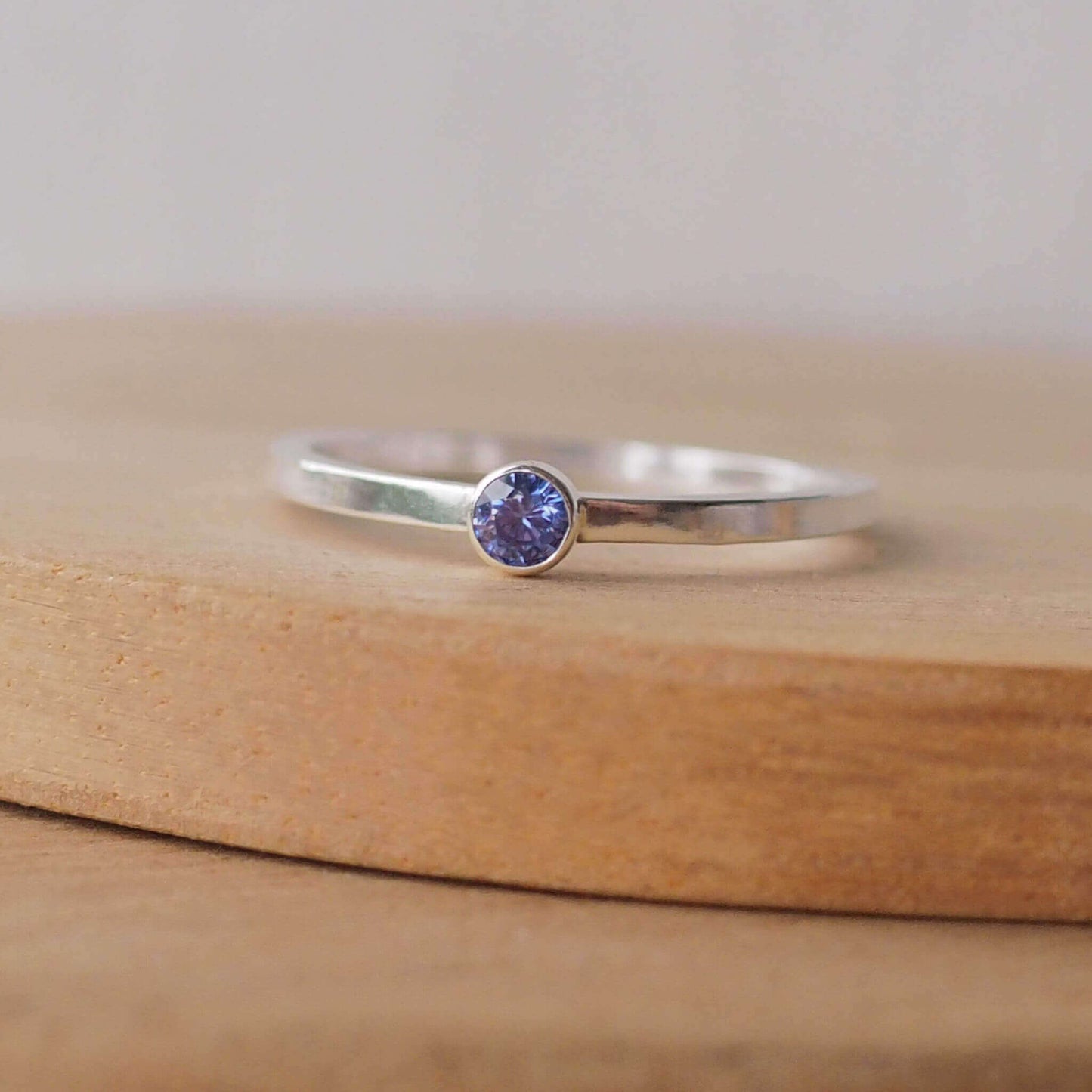 Simple Solitaire ring with a man made tanzanite gemstone. The ring is made from Sterling Silver and a round violet cubic zirconia measuring 3mm in size. It is sent onto a modern ring with a square profile. The ring is handmade by maram jewellery in Scotland