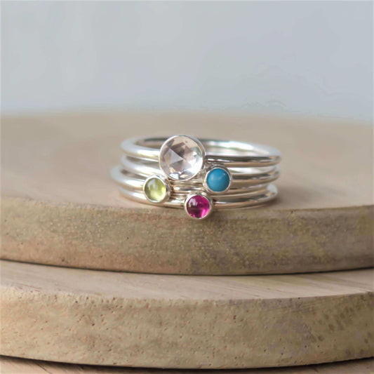 Four ring set of silver rings with different sized gemstones. Includes a 5mm faceted clear topaz, turquoise, peridot and pink lab ruby all 3mm in size. Handmade by maram jewellery in Edinburgh