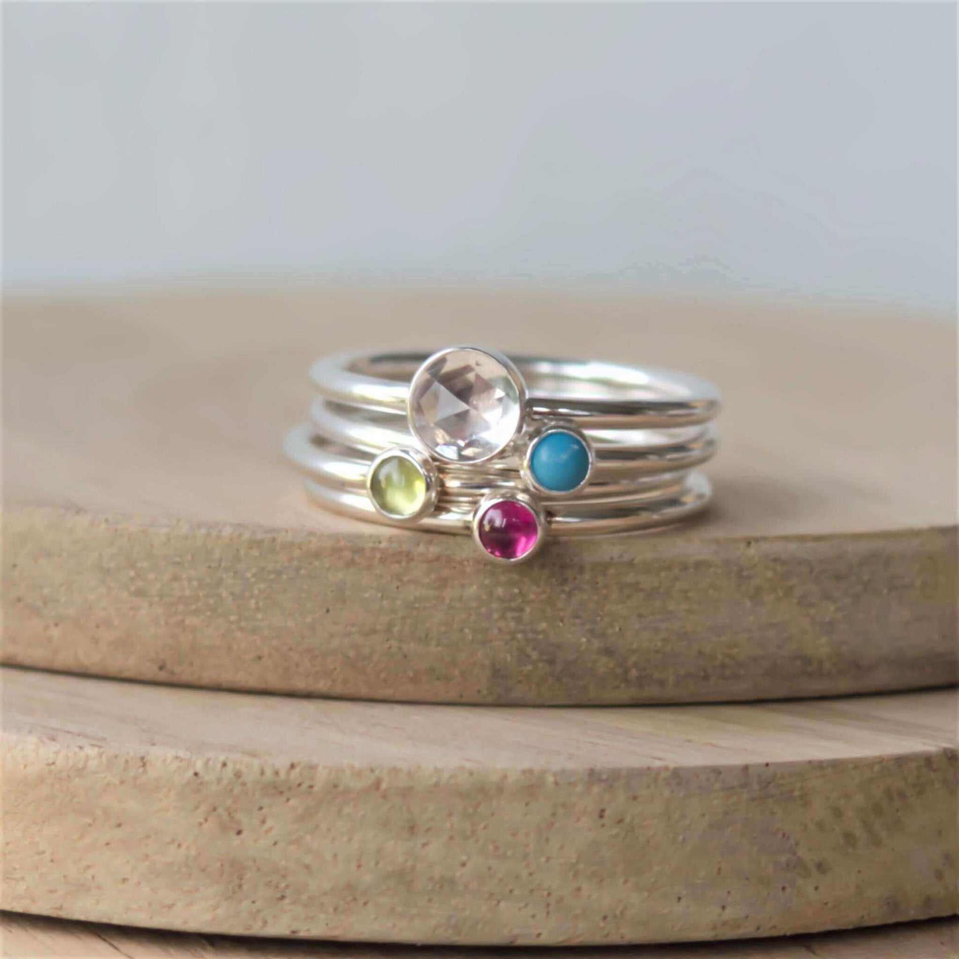 Four ring set of silver rings with different sized gemstones. Includes a 5mm faceted clear topaz, turquoise, peridot and pink lab ruby all 3mm in size. Handmade by maram jewellery in Edinburgh