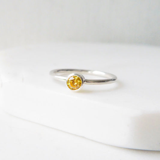 Simple solitaire silver ring with a bezel set yellow citrine cubic zirconia gemstone. the ring is minimalist in style and handcrafted by Maram Jewellery. It is pictured on a white background.Made in Scotland