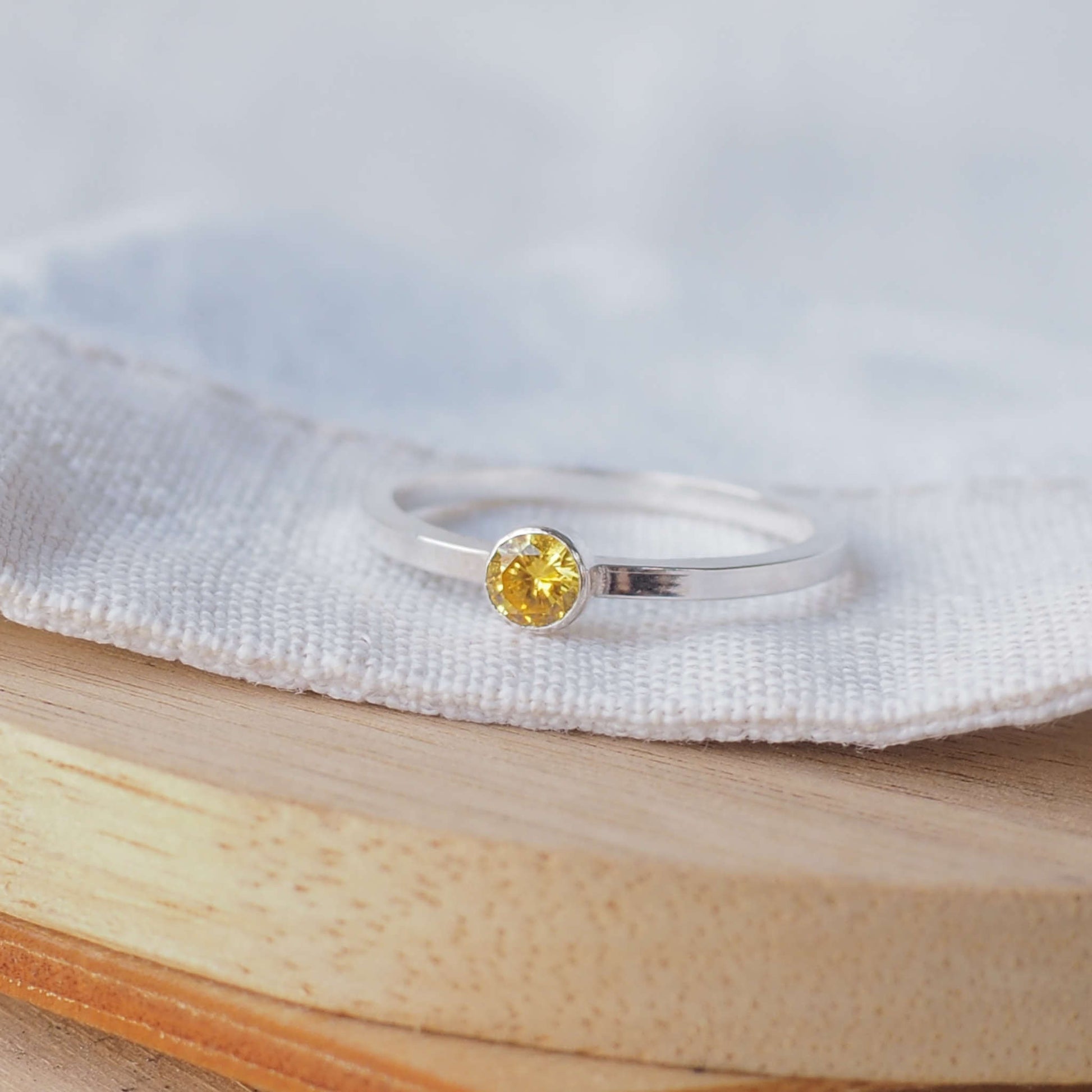 Yellow Sparkly Gemstone ring on a white linen and wood background. The ring is made from white Sterling Silver with a modern square band with a 4mm round bright yellow Cubic Zirconia gemstone. Birthstone for November, Citrine with other birthstones available. Handmade in Scotland by maram jewellery
