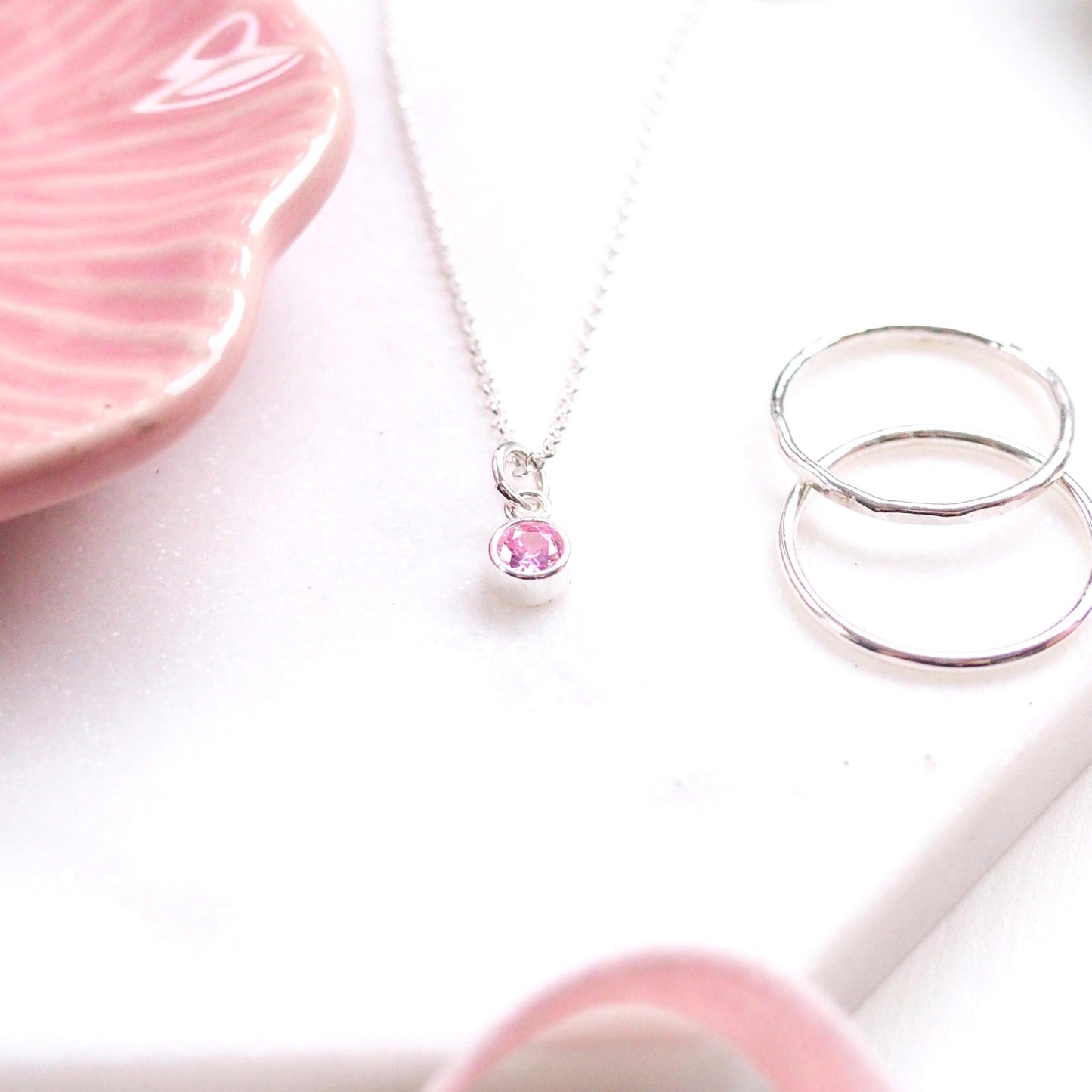 Simple Silver and Cubic Zirconia Pendant in Pale Pink, perfect for a June Birthday as it is the same colour as Alexandrite. The Sterling Silver Pendant in pictured on a white marble background with a pale pink jewellery dish with silver rings. Handcrafted in Scotland by maram jewellery