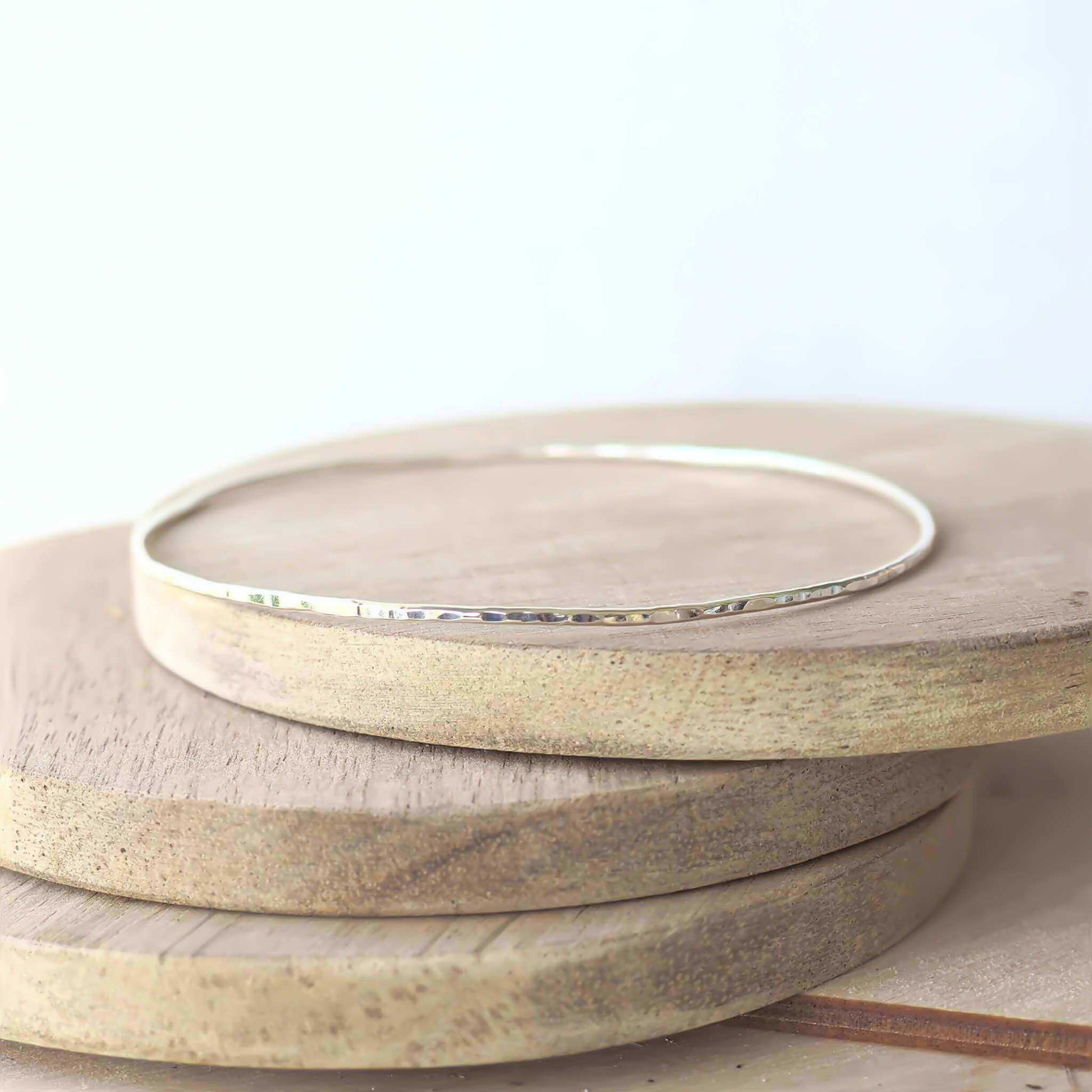 Single Sterling Silver thin hammered bangle handmade in the UK by maram jewellery. pictured on a wood background so that the hammered texture is more visible