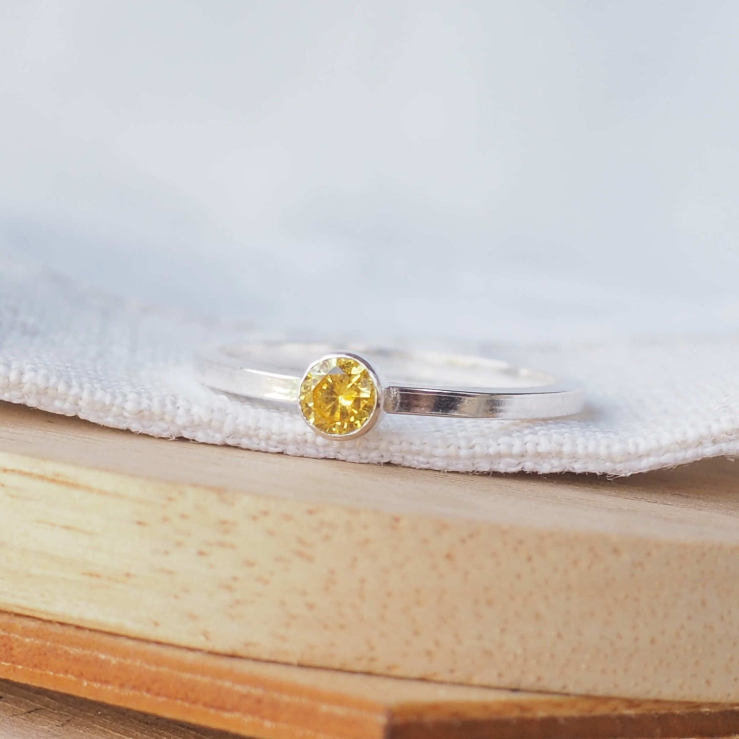 Sparkly yellow gemstone ring on white metal. Sterling Silver and Cubic zirconia ring made in a simple solitaire style with a 4mm round gemstone modern set in a fully enclosed surround. Handmade in Scotland by maram jewellery