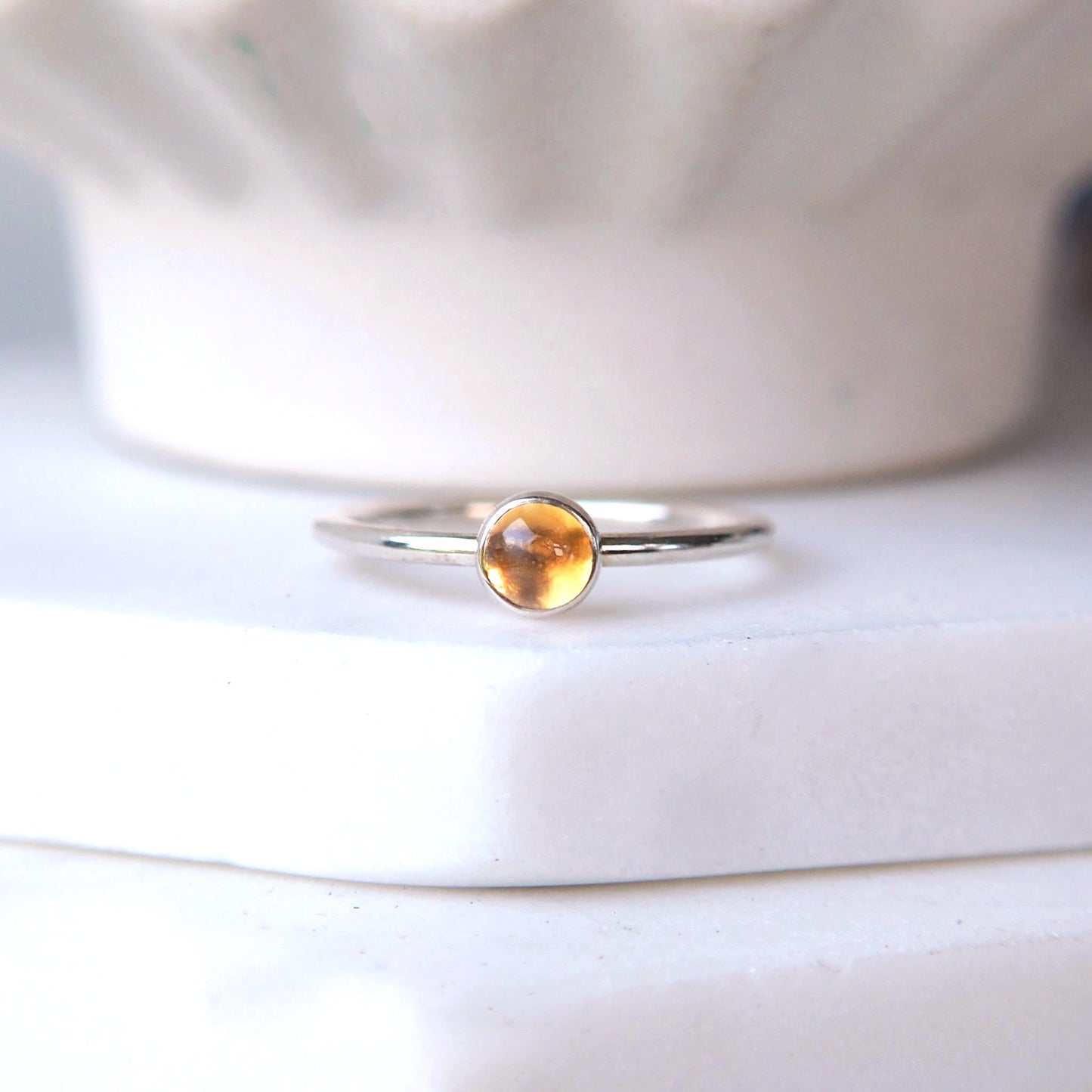 Citrine and Silver simple round gemstone ring pictured on a white marble tile with a cream pot in the background. The ring in a round band with a simple setting holding a 5mm Citrine cabochon. The ring is handmade by maram jewellery in Edinburgh