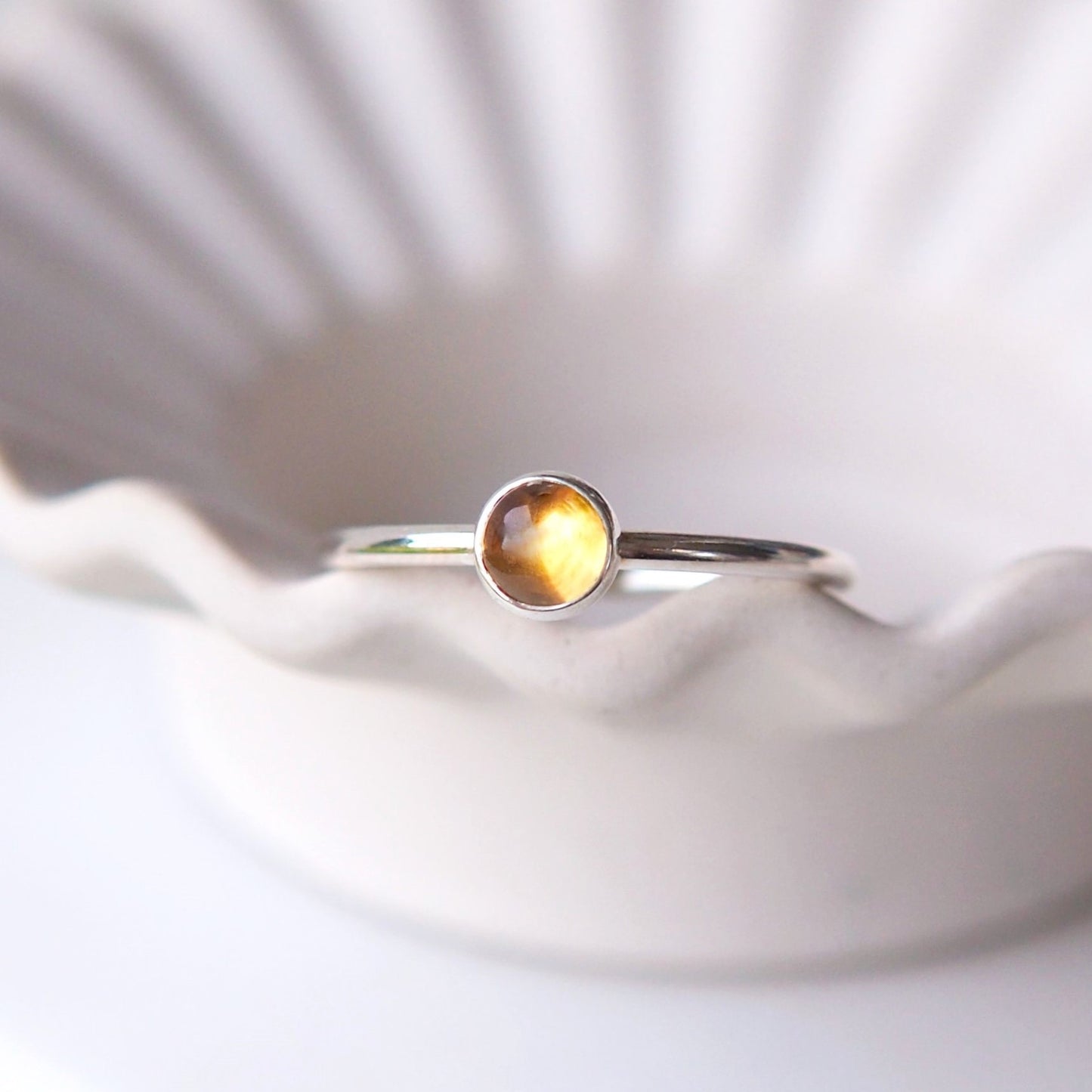 Yellow Citrine gemstone ring in a simple silver ring with a round band in a minimalist style. The ring is pictured sitting on the edge of a wavy bowl. Handmade by maram jewellery in Edinburgh