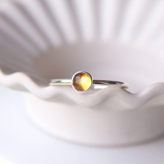 Yellow Citrine gemstone ring in a simple silver ring with a round band in a minimalist style. The ring is pictured sitting on the edge of a wavy bowl. Handmade by maram jewellery in Edinburgh