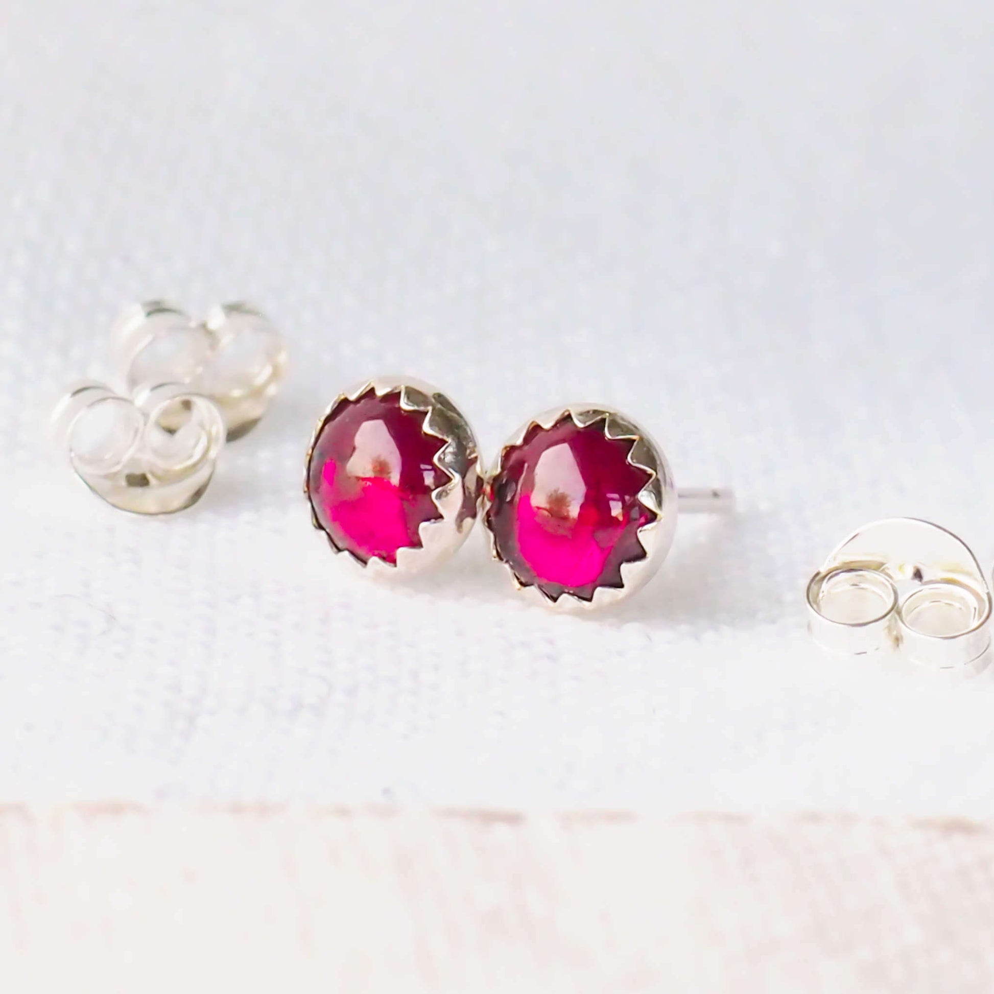 Simple gemstone stud earrings made with a pair of rich red round 5mm cabochon cut garnets set into simple silver mounts. handcrafted by maram jewellery, a small independent jeweller in Scotland UK