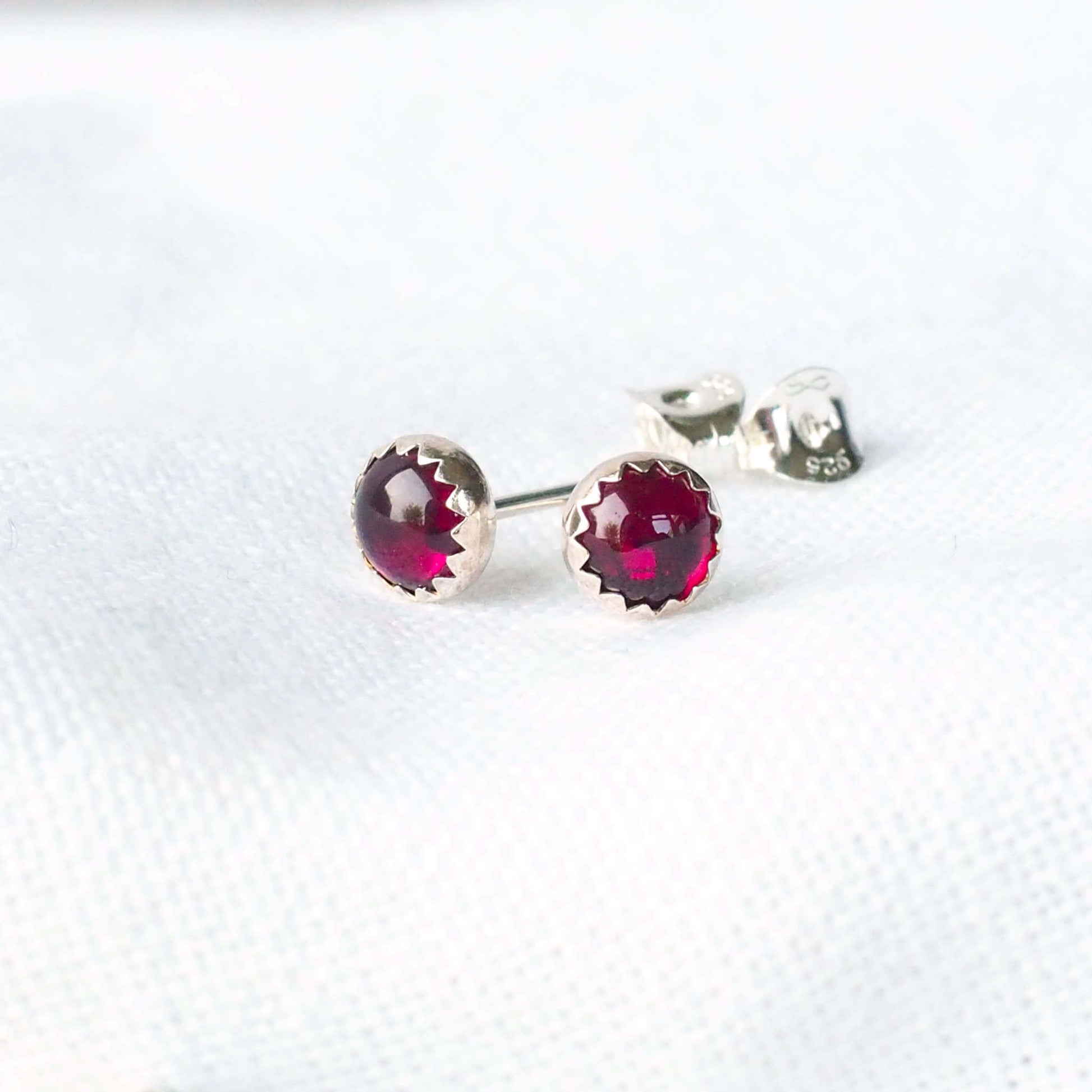 Simple Modern Gemstone stud earrings in sterling silver and round garnet. The earrings measure 5mm in size and are very simply set with a unusual wavy edge. Handmade in Scotland by a small independent jeweller called maram jewellery