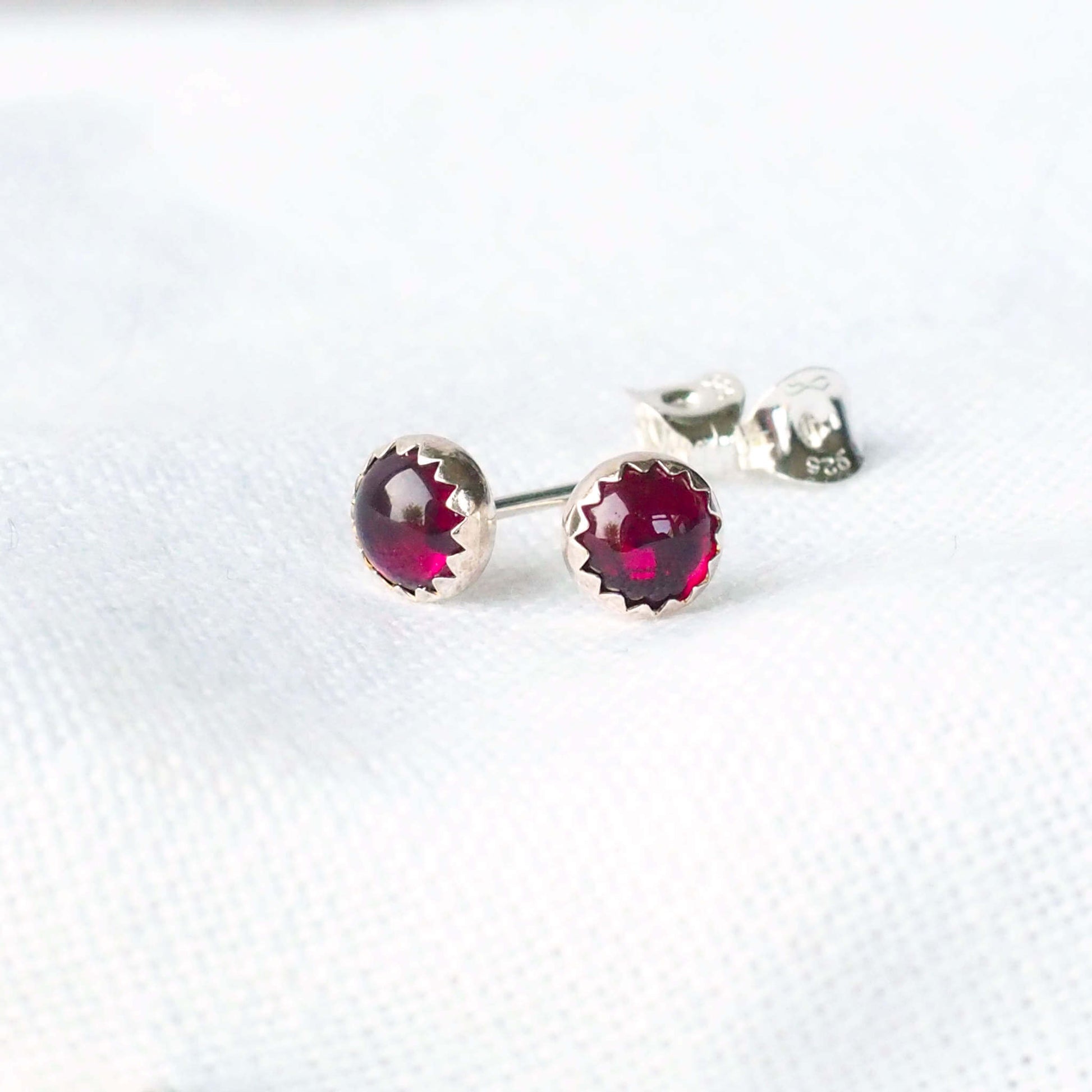Simple gemstone stud earrings made with a pair of rich red round 5mm cabochon cut garnets set into simple silver mounts. handcrafted by maram jewellery, a small independent jeweller in Scotland UK