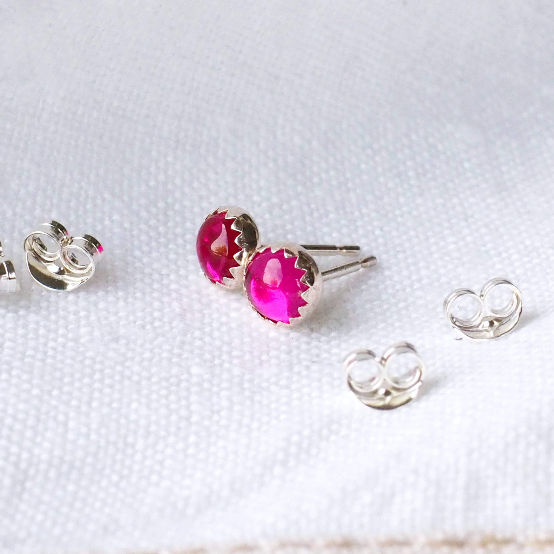 Pair of Hot Pink and SIlver Gemstone studs with a round cabochon gemstone set into a simple sterling silver mount. the earrings are round measuring 5 mm in diameter and are pictured on a white linen background with earring backs at the side. Handcrafted by maram jewellery in Scotland