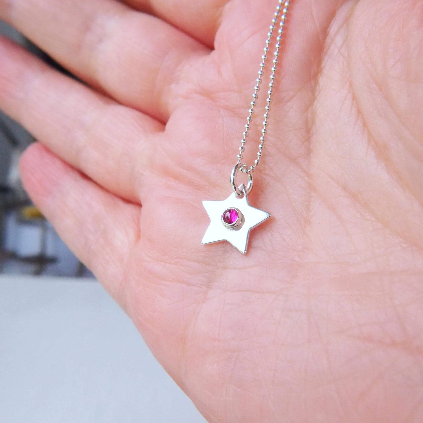 Star Birthstone Charm Necklace with a round 3mm lab ruby cabochon centre. Measuring 12mm in size so is small enough for children as well as adults and is available in a range of other birthstones too. It is Sterling Silver and comes with a choice of chain design and length.The gemstone is Lab Ruby, Birthstone for July. Handmade in Scotland by Maram Jewellery