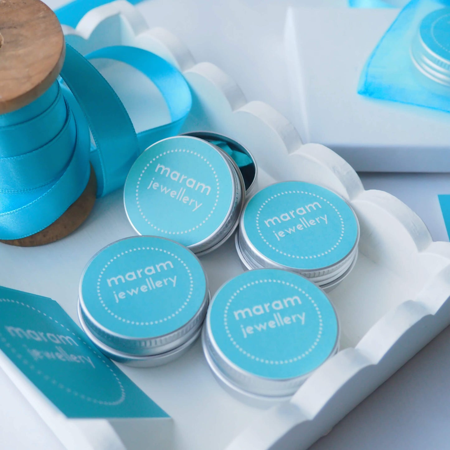 maram jewellery packaging. Small round aluminium tins with turquoise lid with maram jewellery logo. Recyclable and designed for reuse