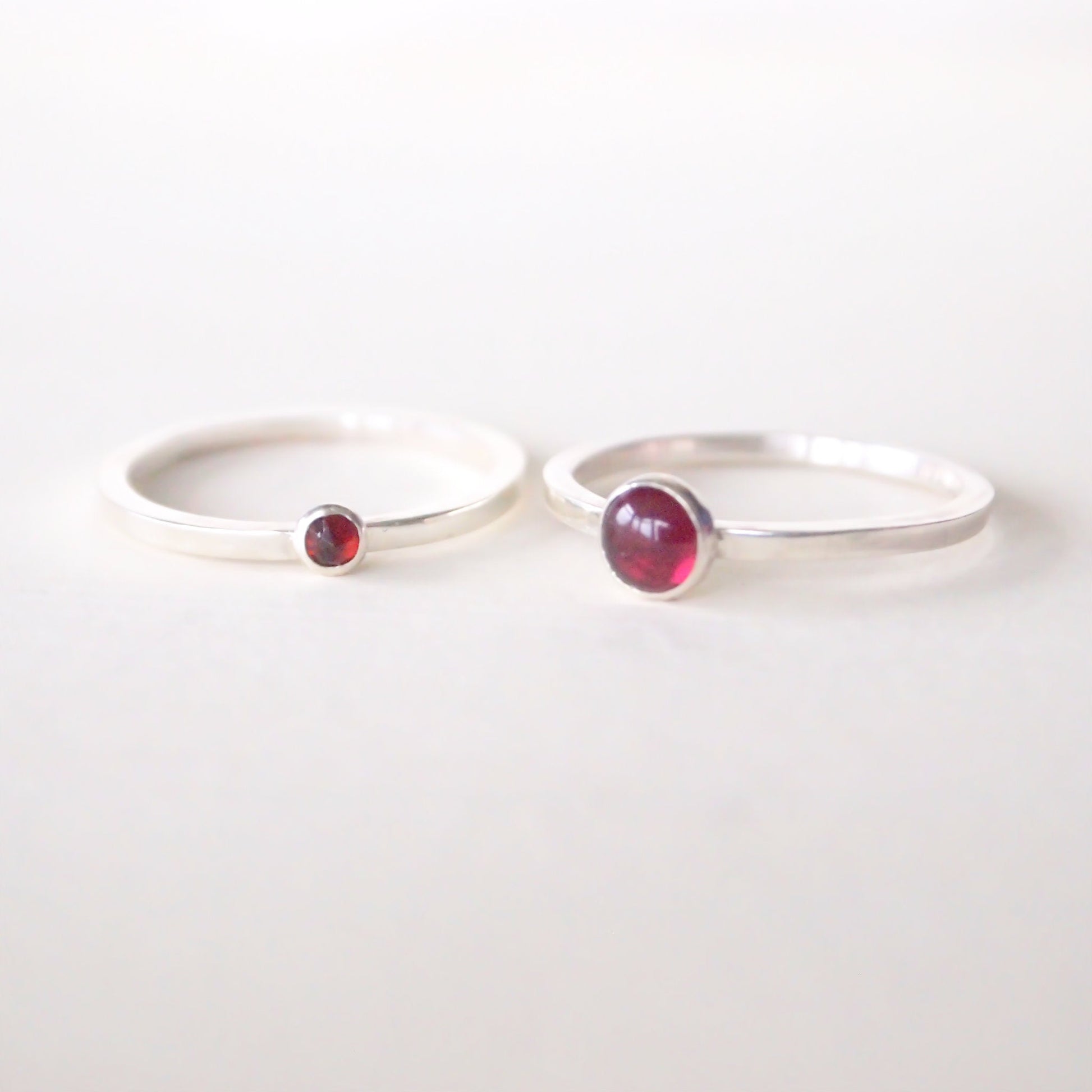 Two Sterling Silver and garnet rings side by side, one with a 5mm round gem and on with a 3mm round faceted gemstone. modern birthstones rings that can be stacked together, handcrafted by maram jewellery in Scotland UK