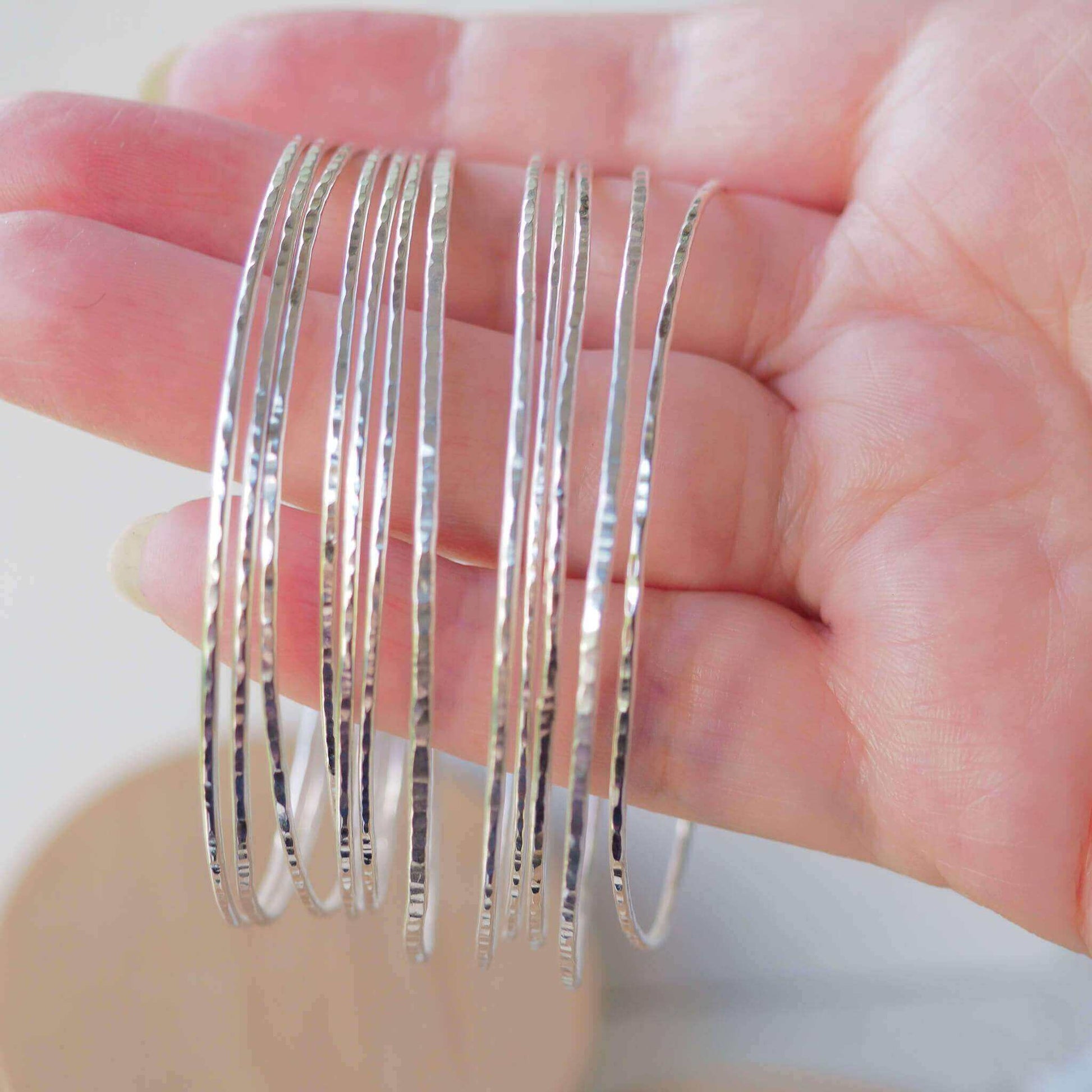 Stack of Sterling Silver Thin Bangles held in hand to show size and hammered texture. Super thin designed for stacking, perfect boho hippy style bangles. Handmade in the UK by Maram Jewellery