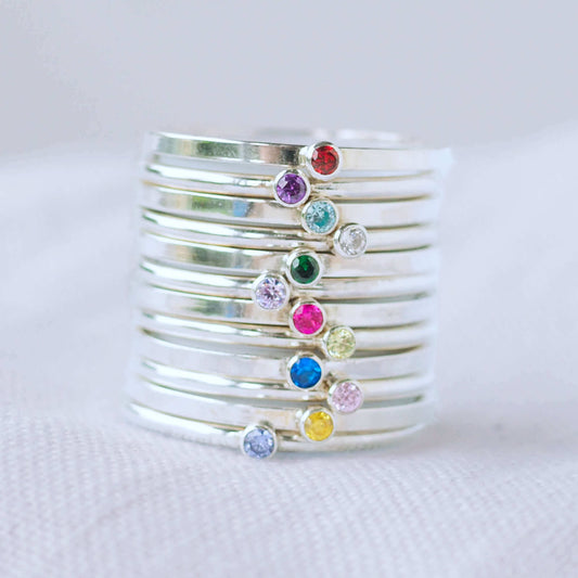 Stack of twelve birthstone rings in Sterling Silver with a round coloured cubic zirconia in 2 mm size to mark birthstones for every month. Rainbow bright coloured gems with round or square silver bands to create a modern minimalist gemstone ring. Handmade in Scotland by maram jewellery
