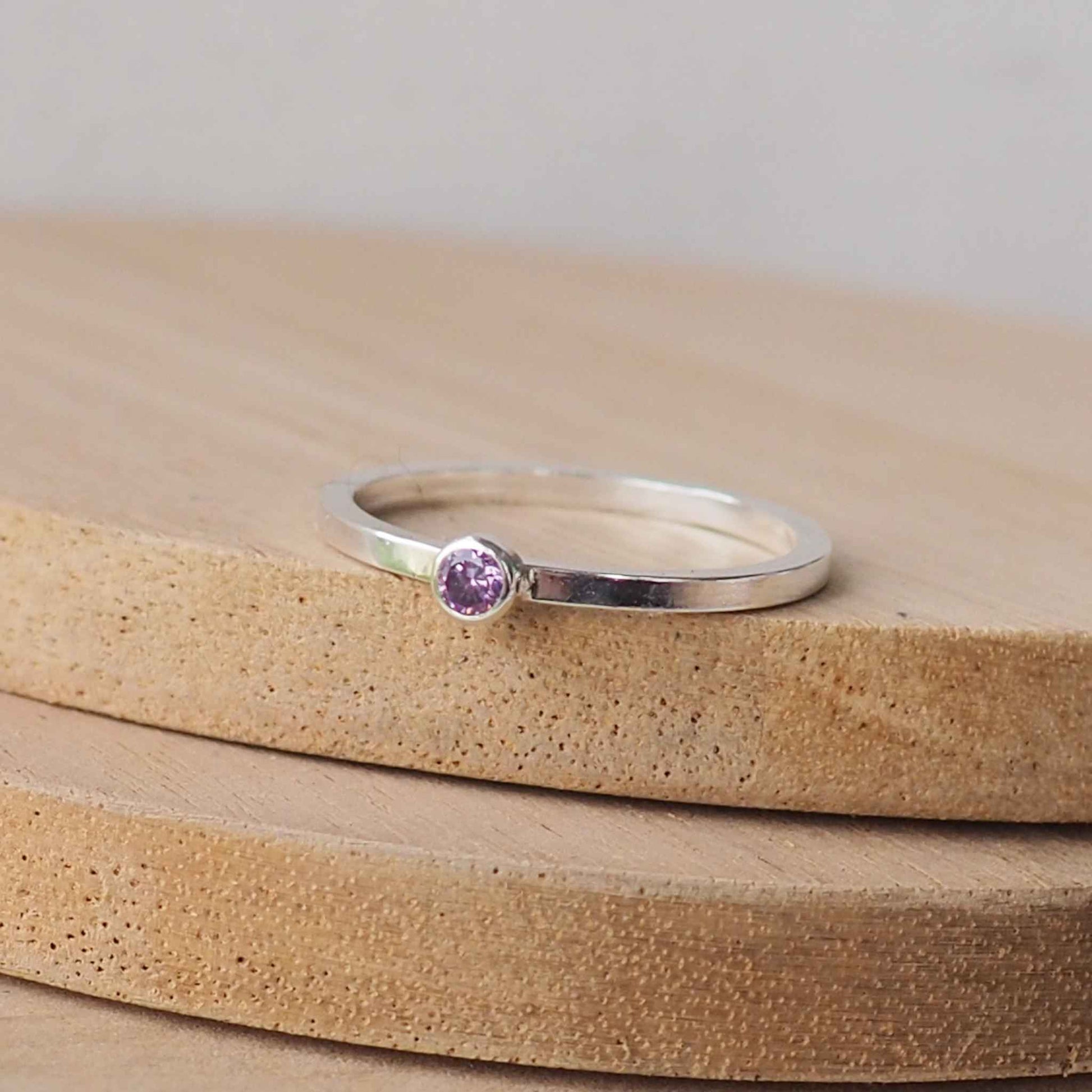 Silver ring with a purple gemstone. The ring is simple in style with no embellishment , with a square wire band 1.5mm thick with a simple Purple Amethyst 2mm round cubic zirconia stone set in an enclosed silver setting. The gem is very small and minimal on the band. Amethyst is birthstone for February. The ring is Sterling Silver and made to your ring size. Handmade in Scotland by Maram Jewellery