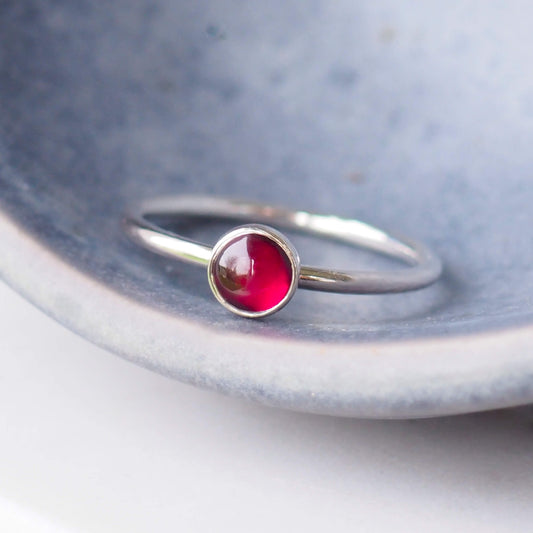 Garnet 5mm round cabochon ring in silver on a rich grey ceramic background. handmade in Scotland by maram jewellery